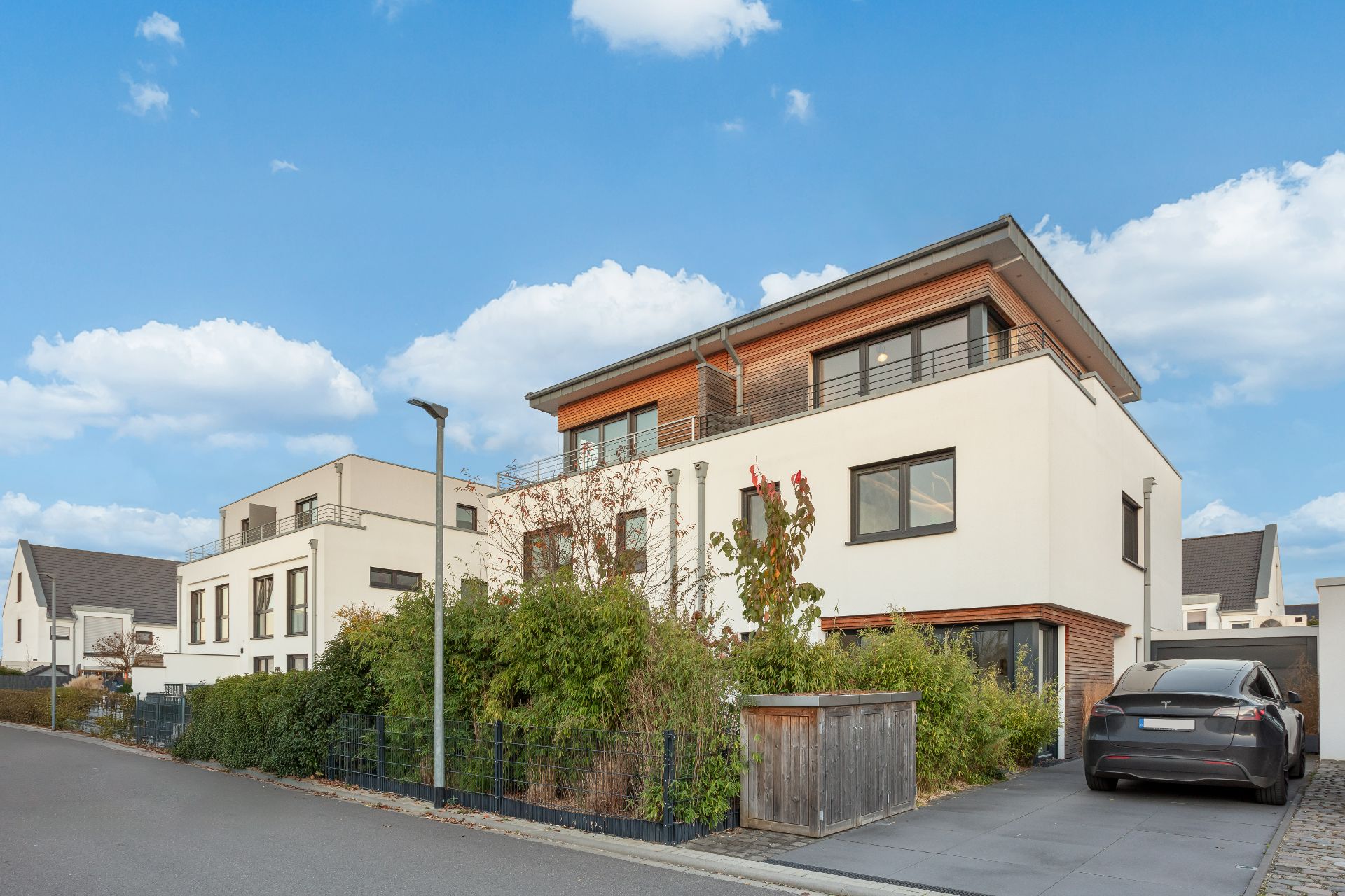 Modernes Wohnhaus mit Flachdach, Vorgarten, Zaun und geparktem Auto in Einfahrt.