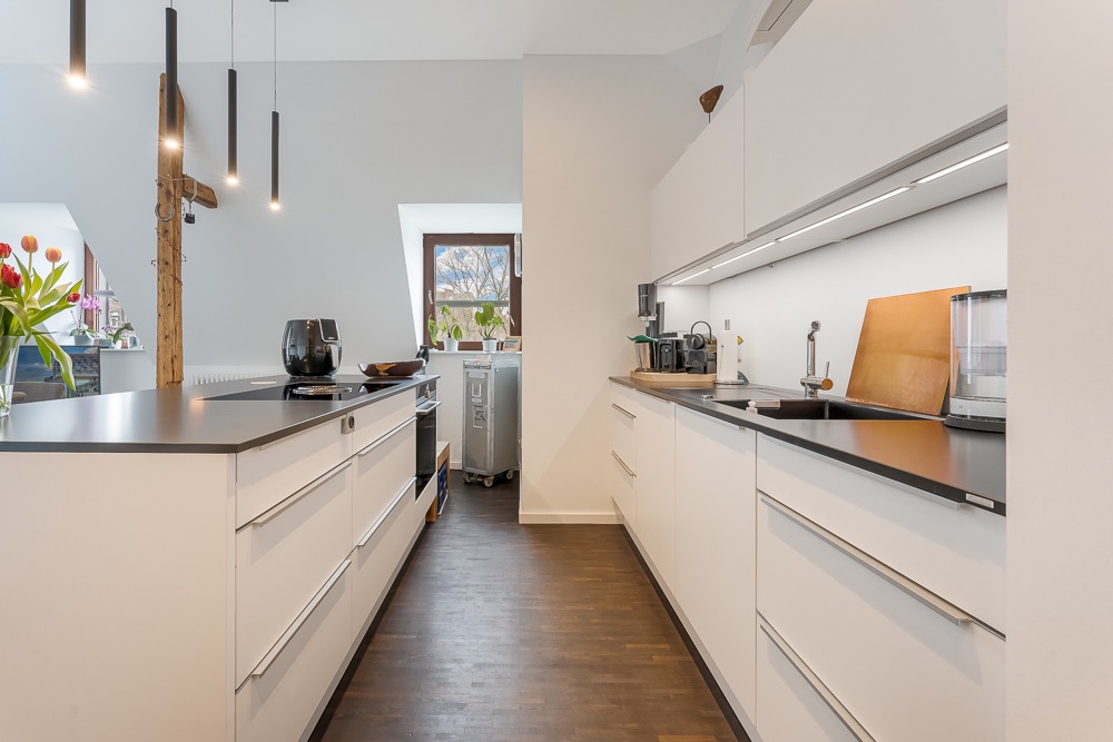 Moderne Küche mit weißen Schränken, Kochinsel und Holzfußboden, helle Beleuchtung.