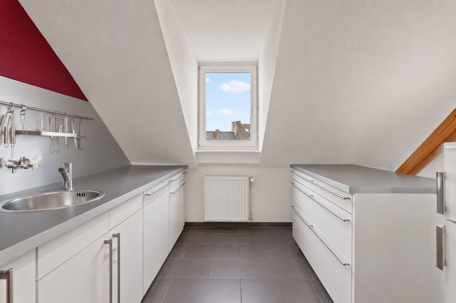 Moderne Dachgeschossküche mit weißen Schränken, grauen Arbeitsplatten und Fenster mittig.