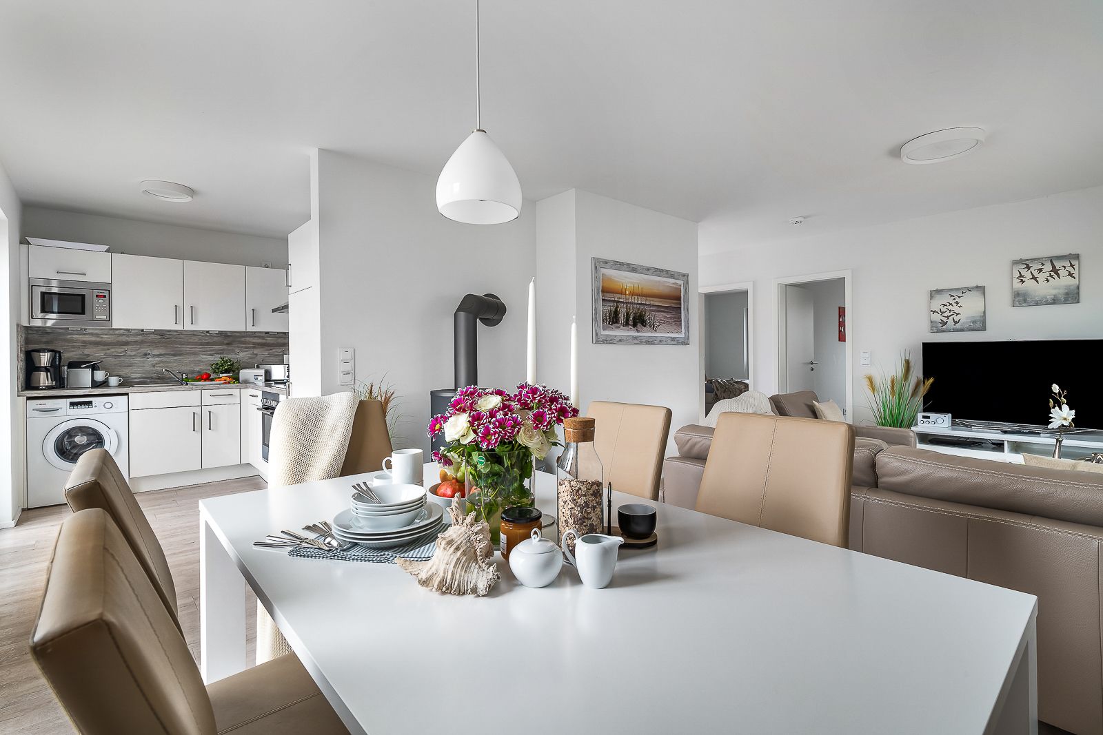 Heller Essbereich mit gedecktem Tisch, angrenzender offener Küche und Wohnzimmer im Hintergrund.