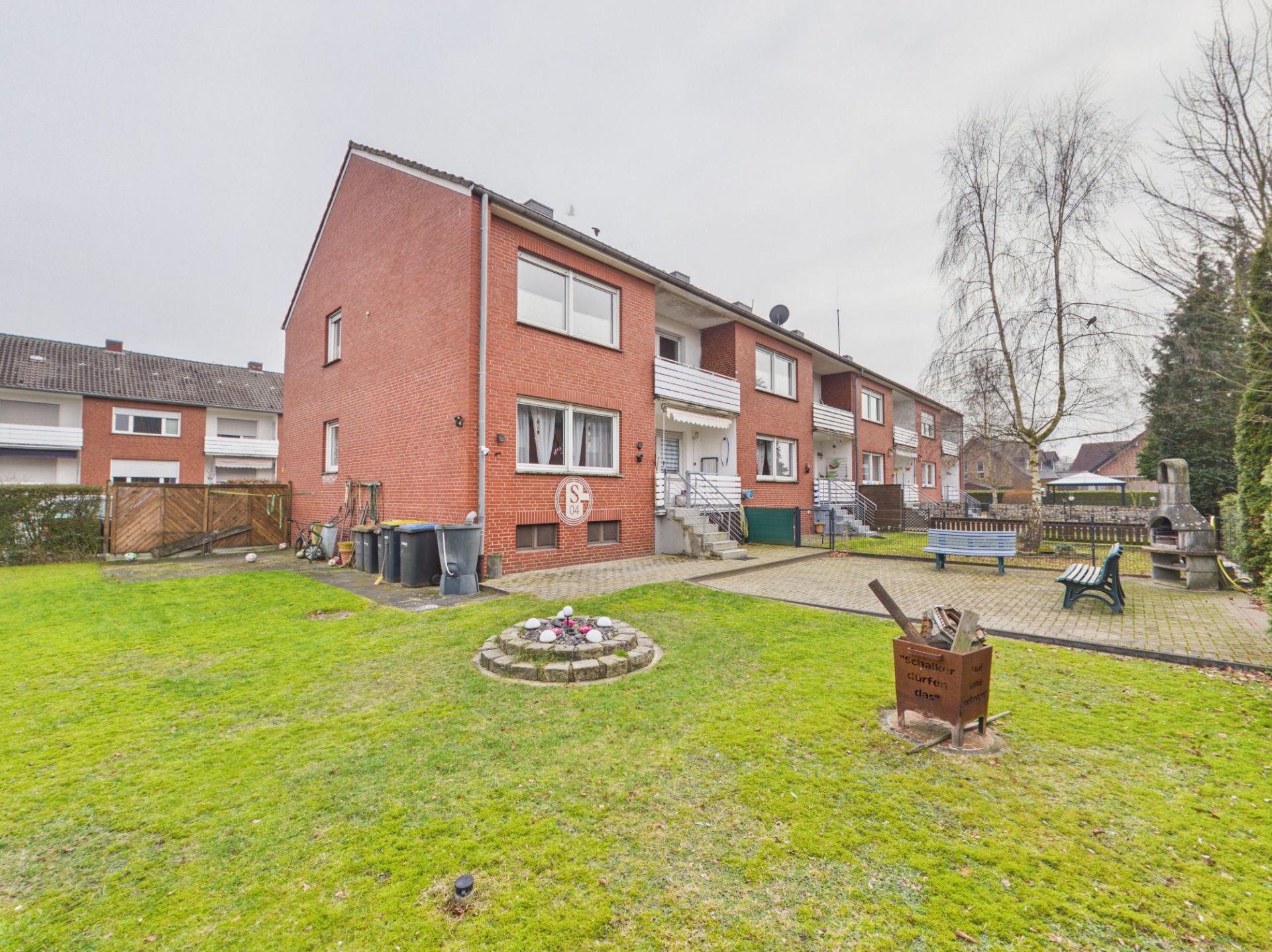 Reihenhaus mit roter Fassade, großem Garten, Bänken und Feuerstelle im Außenbereich.