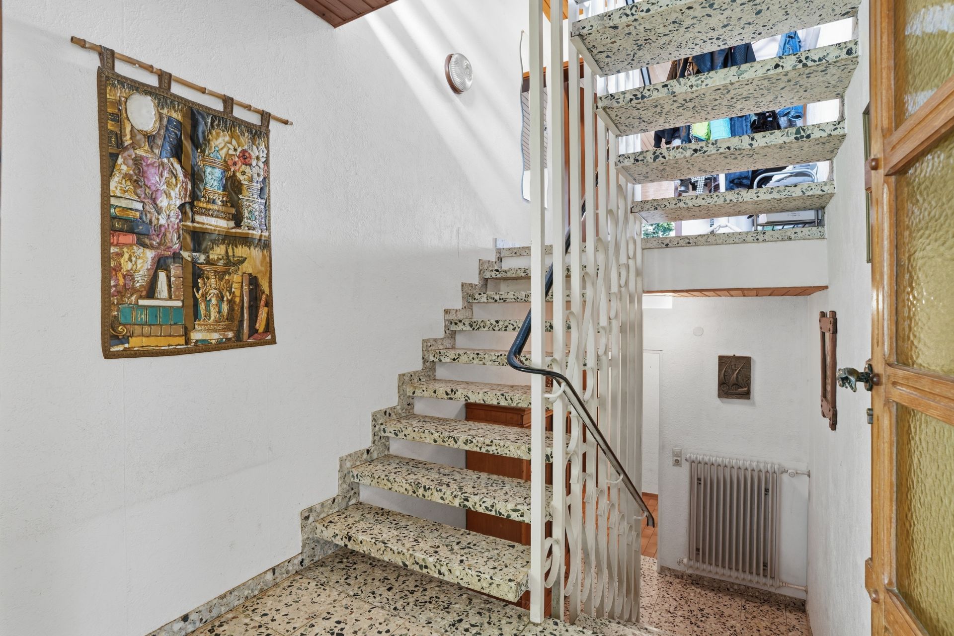 Helle Innentreppe mit Kunst an der weißen Wand und Handlauf aus Metall.