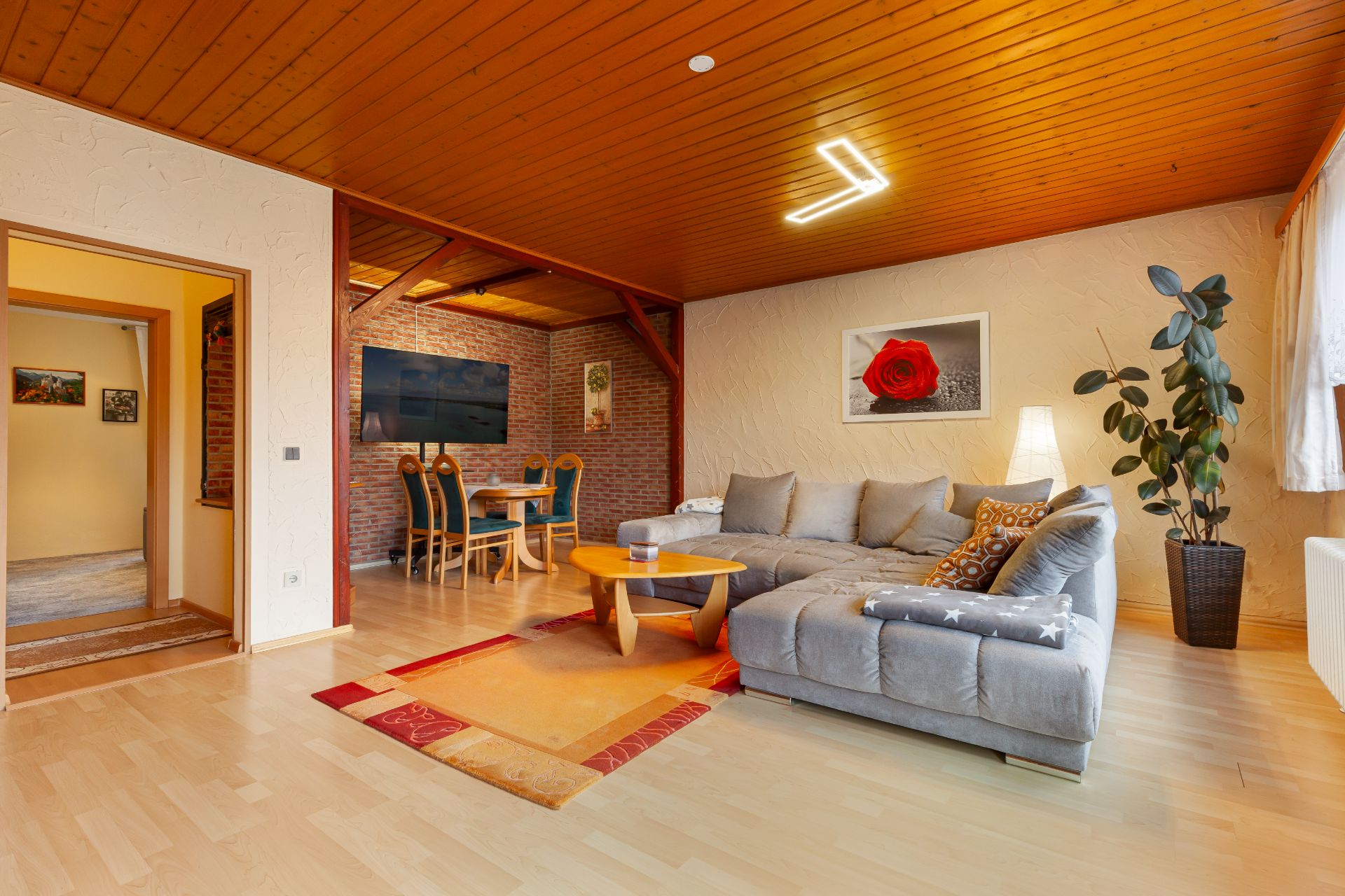 Wohnzimmer mit grauem Sofa, Holztisch, Pflanze und Essbereich im Hintergrund.