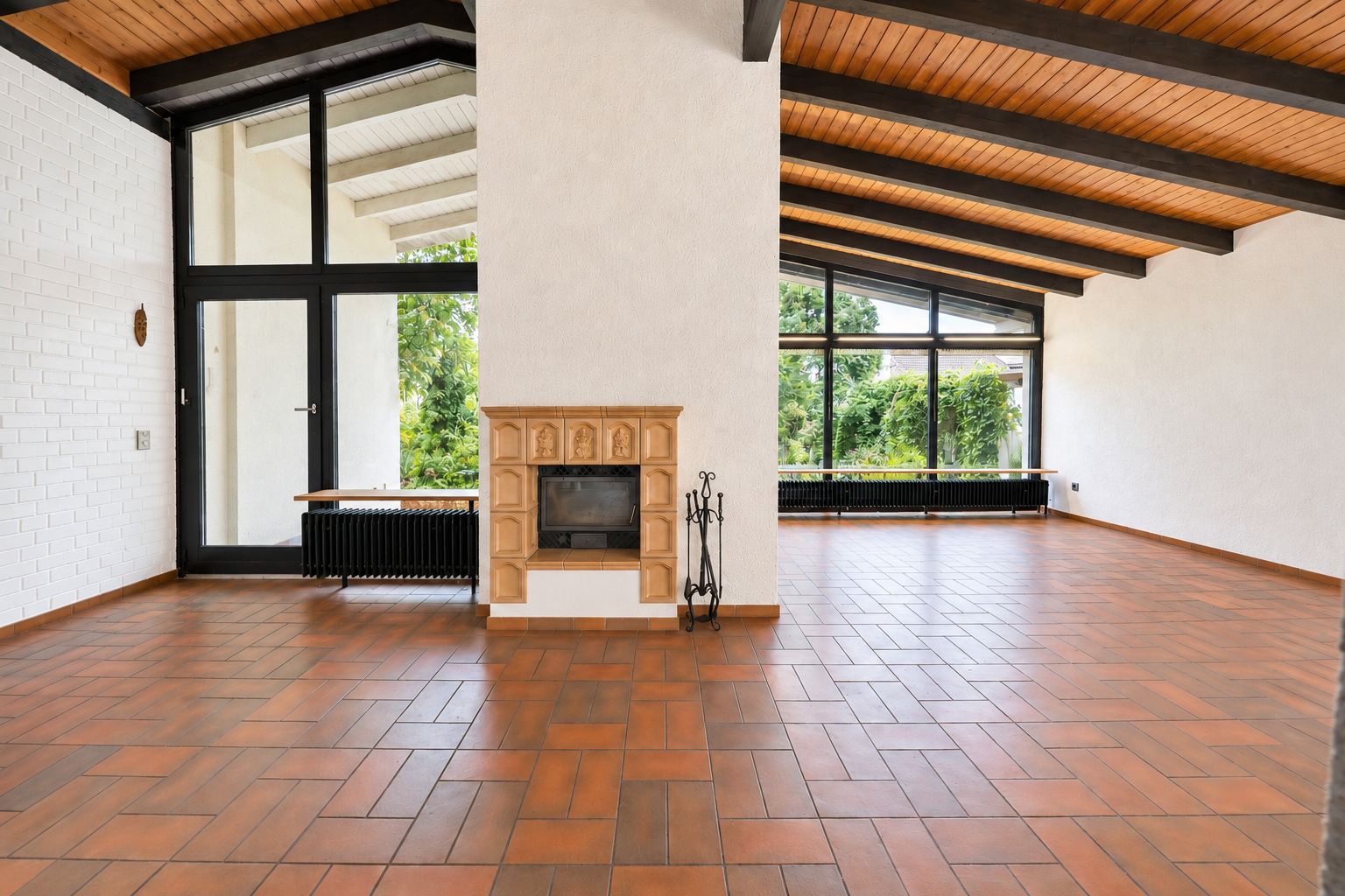 Helles Wohnzimmer mit Kamin, großen Fenstern und sichtbaren Holzbalken an der Decke.