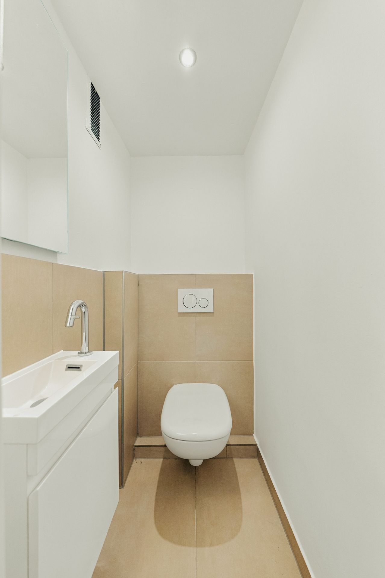 Kleines Badezimmer mit Wand-WC und Waschtisch, hell gefliest und minimalistisch gestaltet.