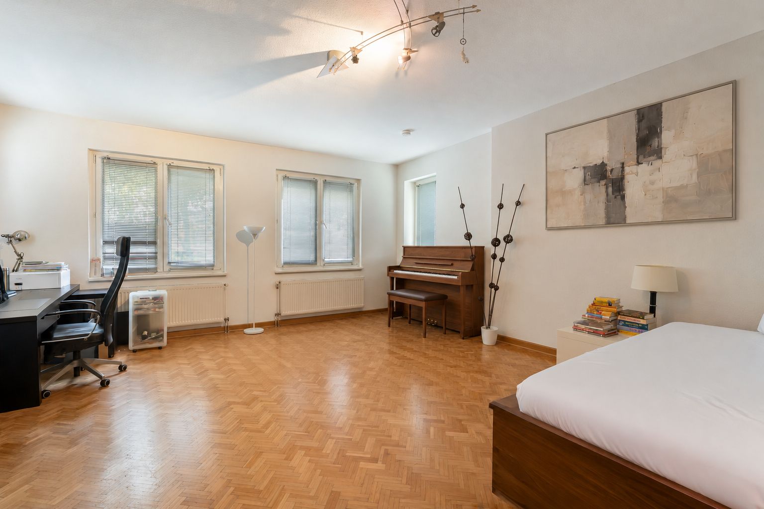 Helles Zimmer mit Schreibtisch, Klavier, Bett und modernen Möbeln auf Parkettboden.