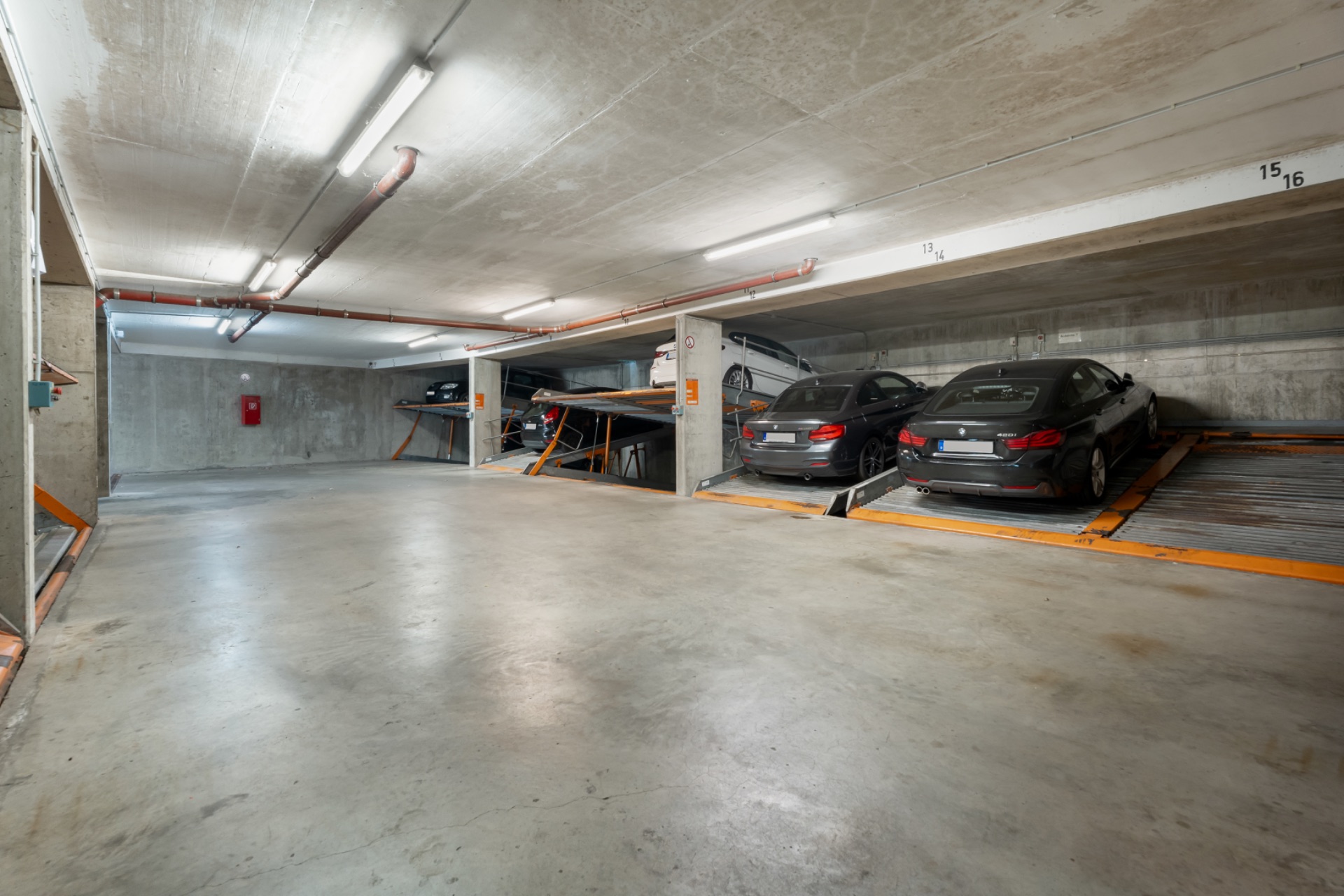 Helle Tiefgarage mit mehreren geparkten Autos und Betonwänden.