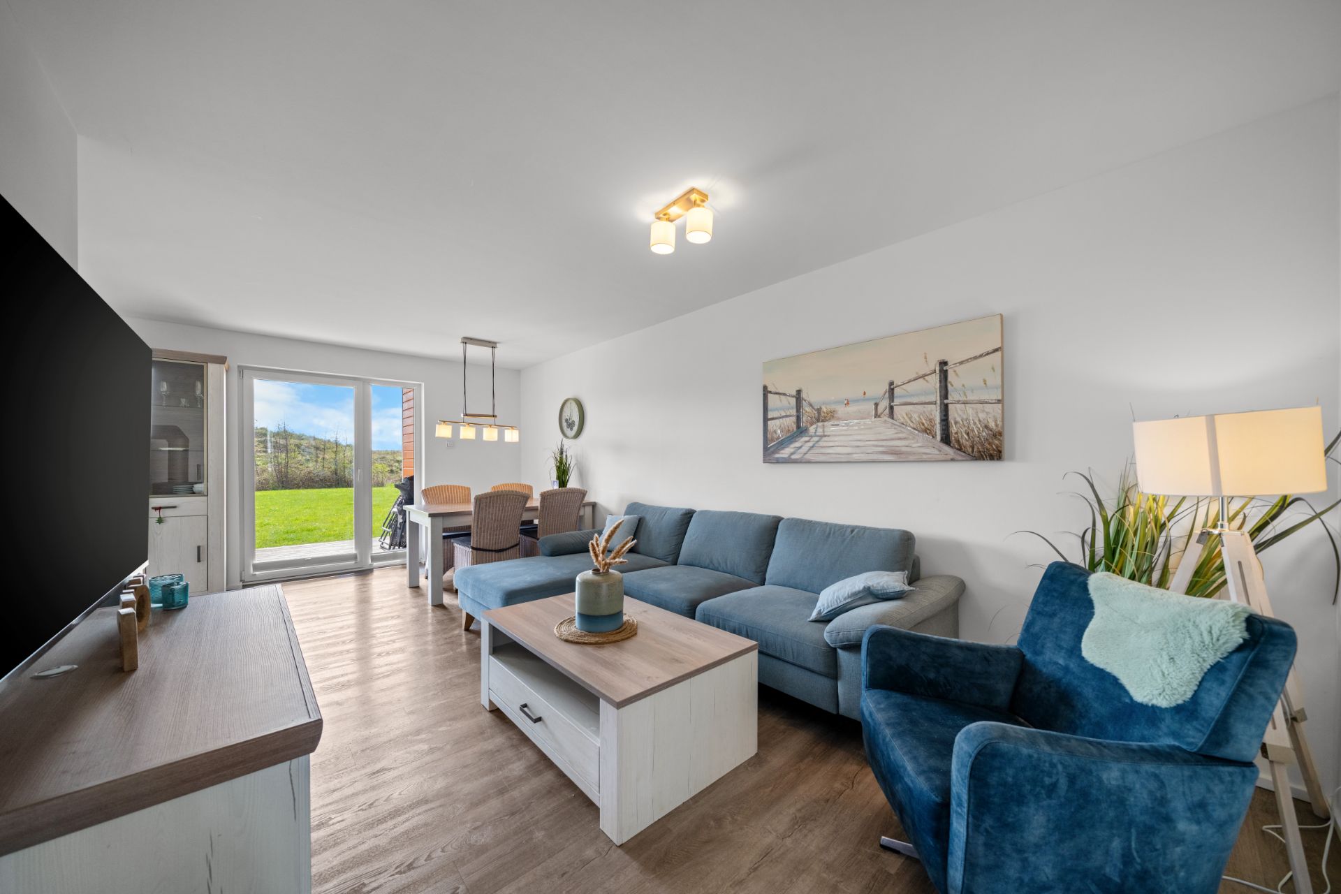 Wohnzimmer mit blauer Couch, Sessel, Couchtisch, Esstisch und Zugang zum Garten.