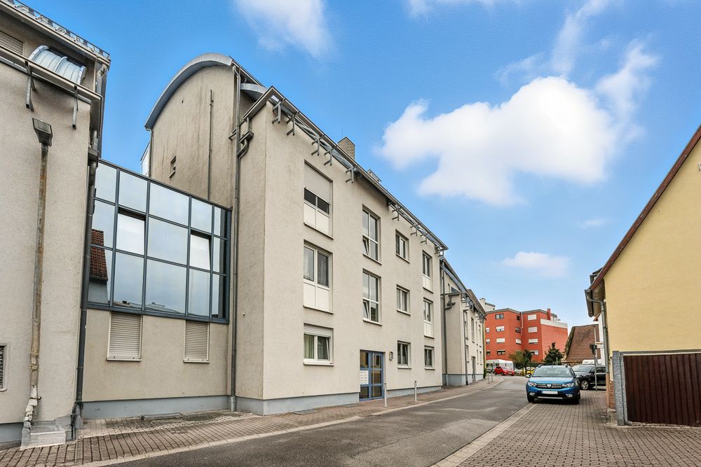 Mehrfamilienhaus mit mehreren Fenstern in einer ruhigen Wohnstraße bei Tageslicht.