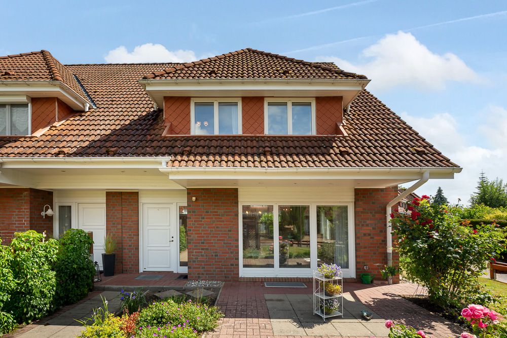 Doppelhaushälfte mit rotem Dach, weißer Tür und Garten im Vordergrund.