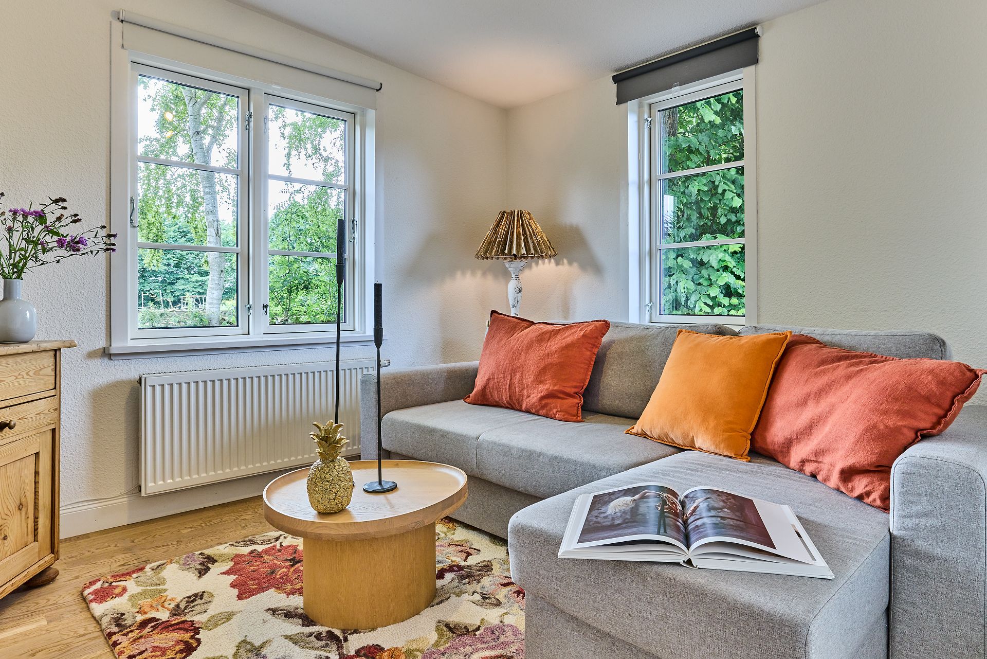 Helles Wohnzimmer mit grauem Sofa, bunten Kissen, Couchtisch und offenem Buch auf dem Sofa.