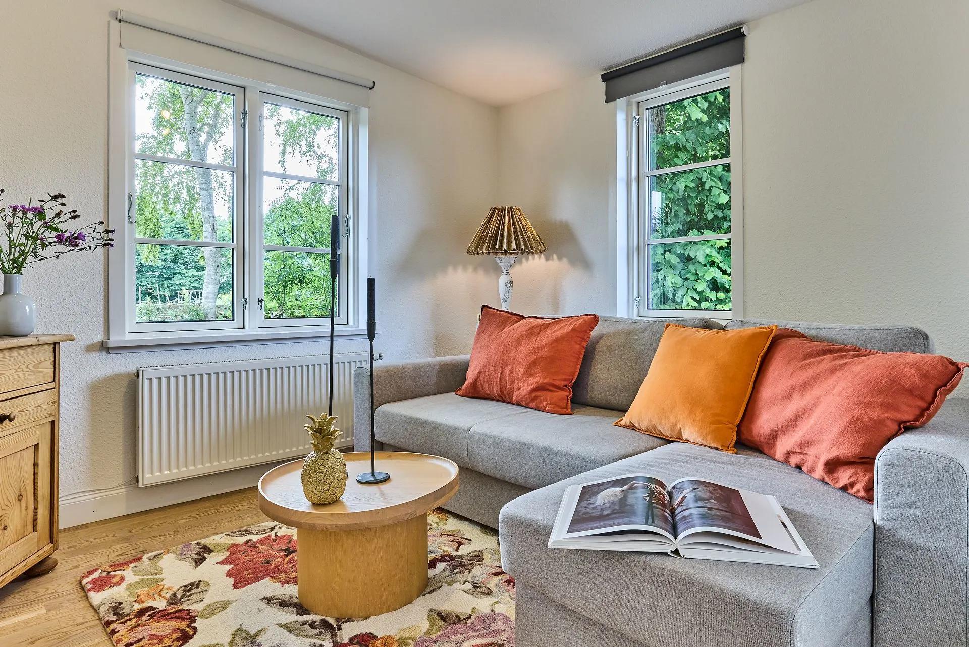 Helles Wohnzimmer mit grauem Sofa, bunten Kissen, Couchtisch und offenem Buch auf dem Sofa.