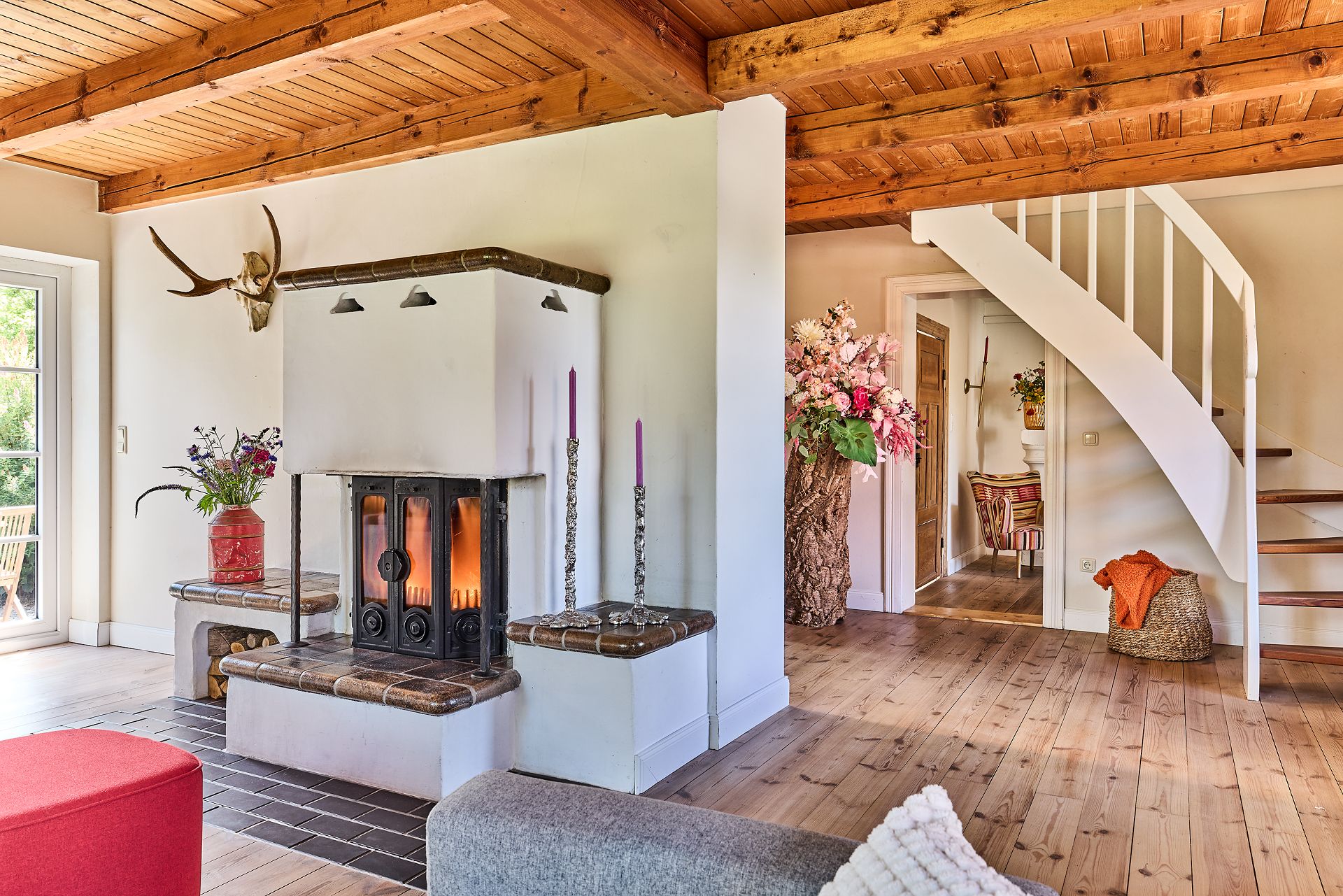 Gemütliches Wohnzimmer mit Kamin, Holzboden, Holzdecke und weißer Treppe.