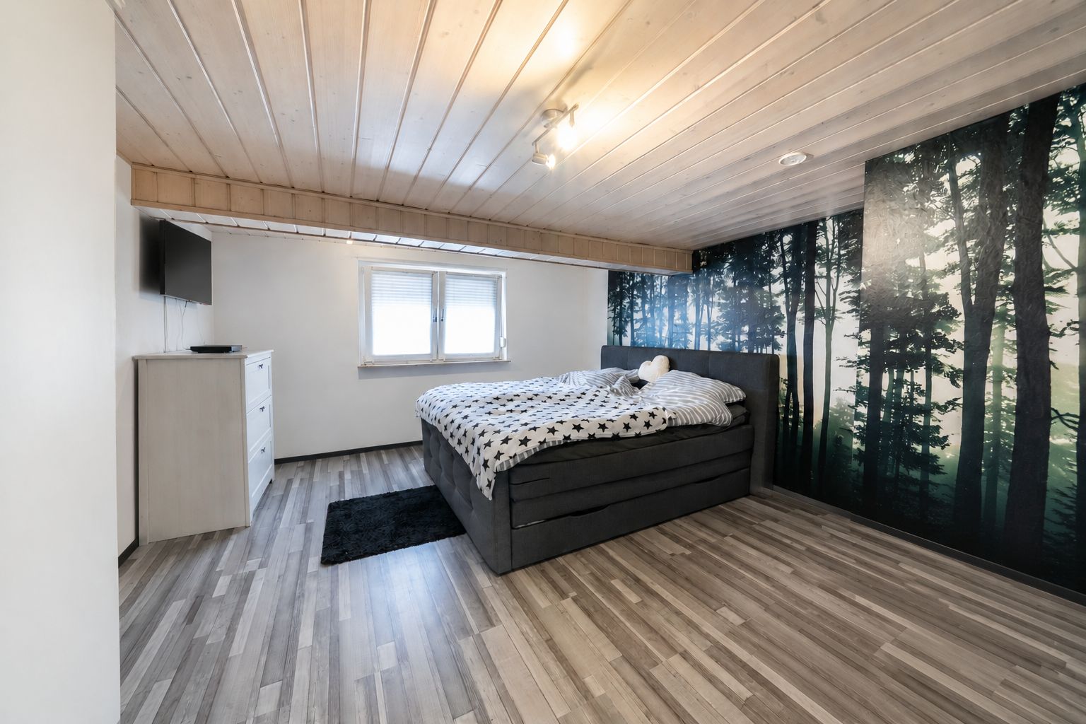 Modernes Schlafzimmer mit Doppelbett, Wandbild eines Waldes und Fenster mit Rollläden.