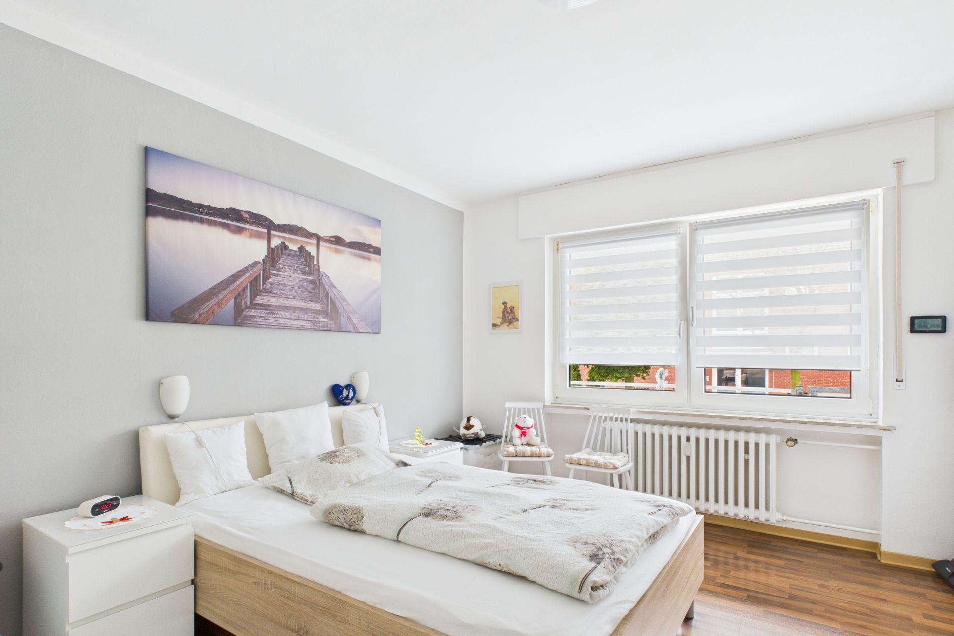 Helles Schlafzimmer mit Doppelbett, zwei Nachttischen, großem Fenster und Wandbild.
