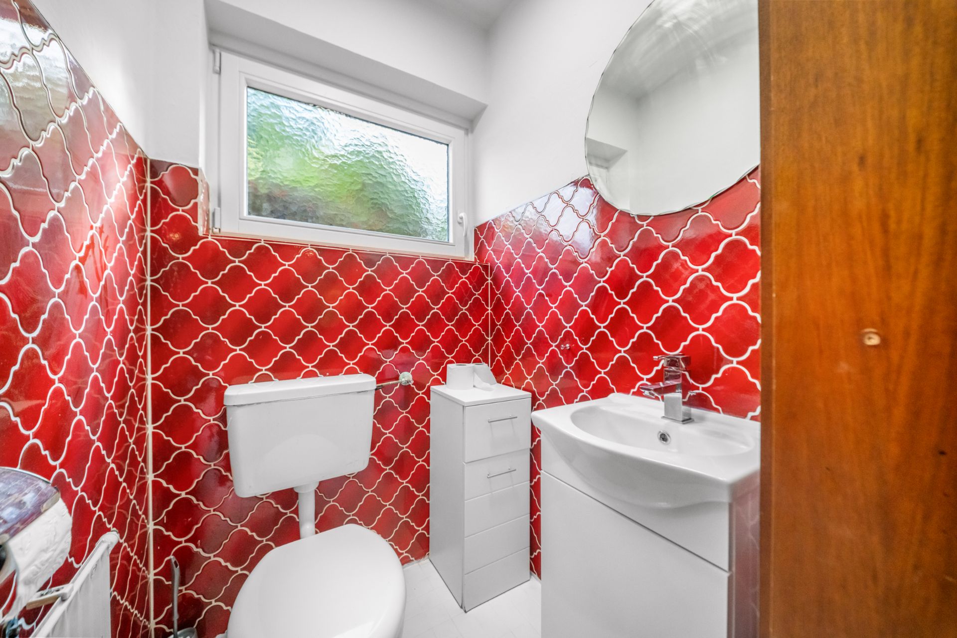 Kleines Badezimmer mit roten Fliesen, WC, Waschbecken, Spiegel und Fenster.