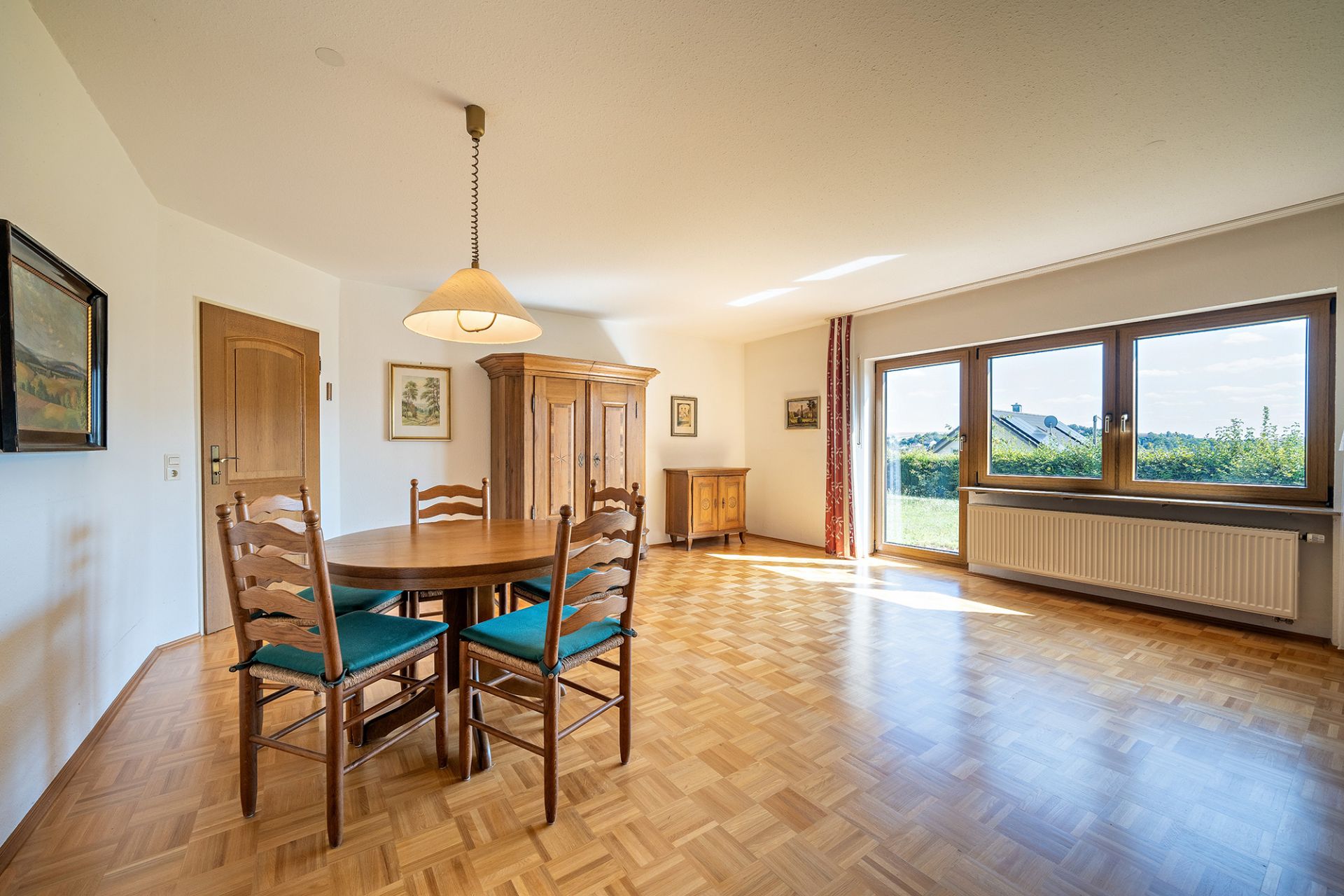 Helles Wohnzimmer mit Esstisch, vier Stühlen, Holzschrank und großem Fenster.