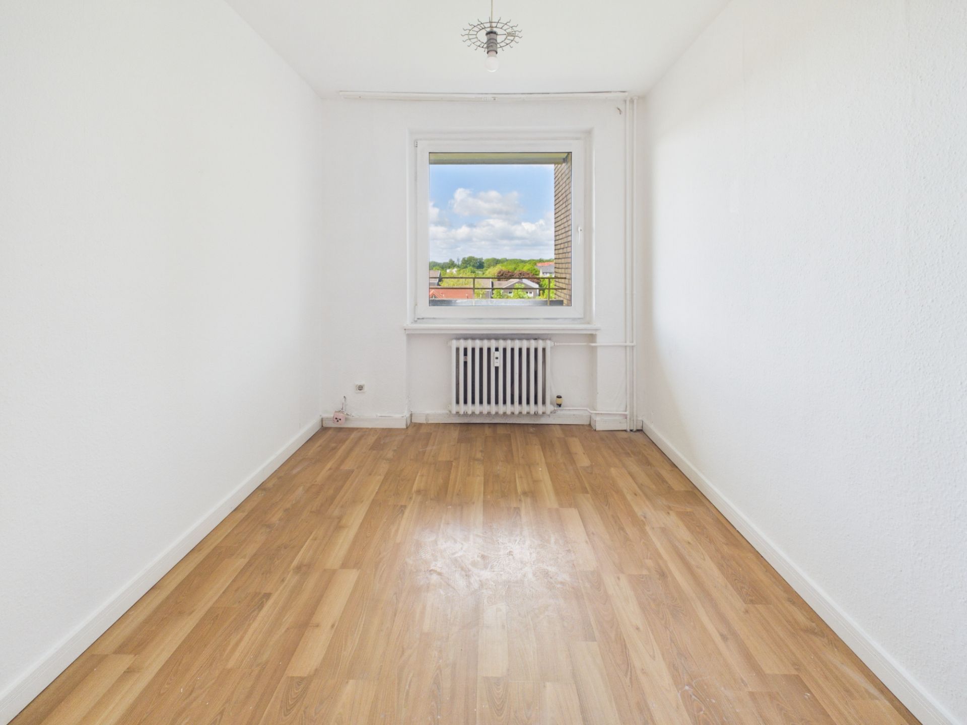 Leerer Raum mit weißer Wand, Holzboden, Fenster und Heizung unter dem Fenster.