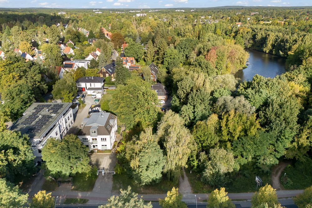 Vogelperspektive auf Wohnhäuser und viele Bäume neben einem See.