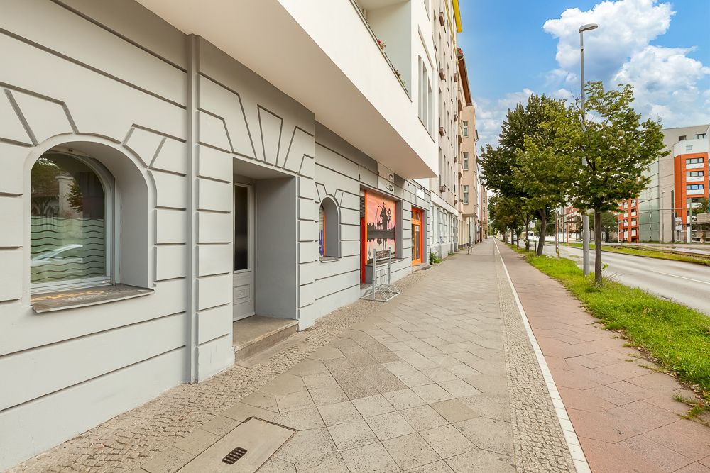 Blick auf den Gehweg und die Fassade eines Wohngebäudes mit Bäumen entlang der Straße.