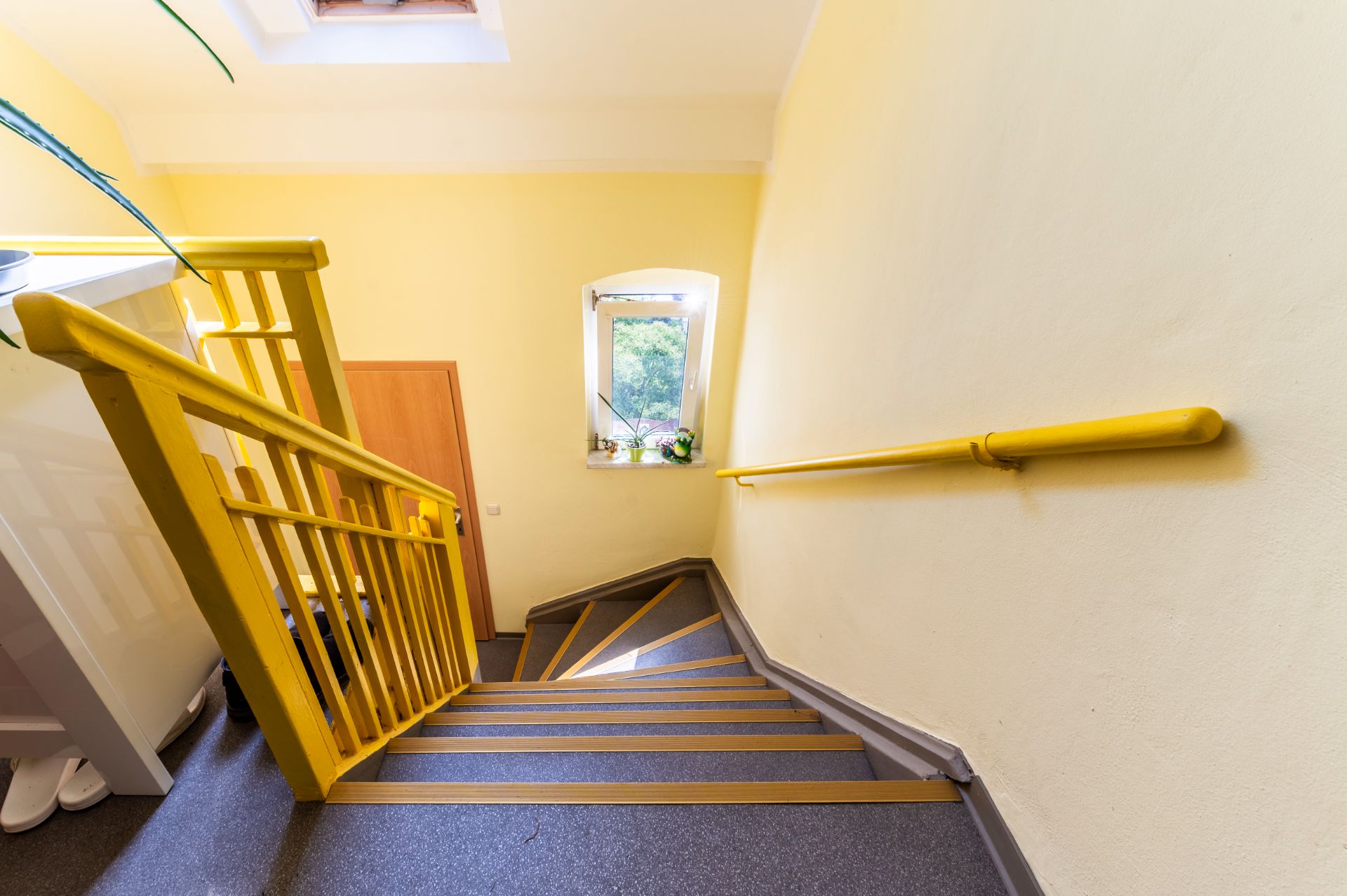 Gelbes Treppengeländer und Handlauf an einer Treppe in einem hellen Wohnhausflur mit Fenster und Tür.
