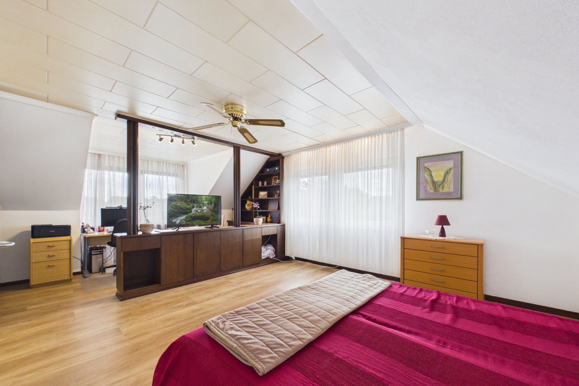 Schlafzimmer mit roter Decke, Deckenventilator, Holzmöbeln und großem Fenster mit Vorhängen.
