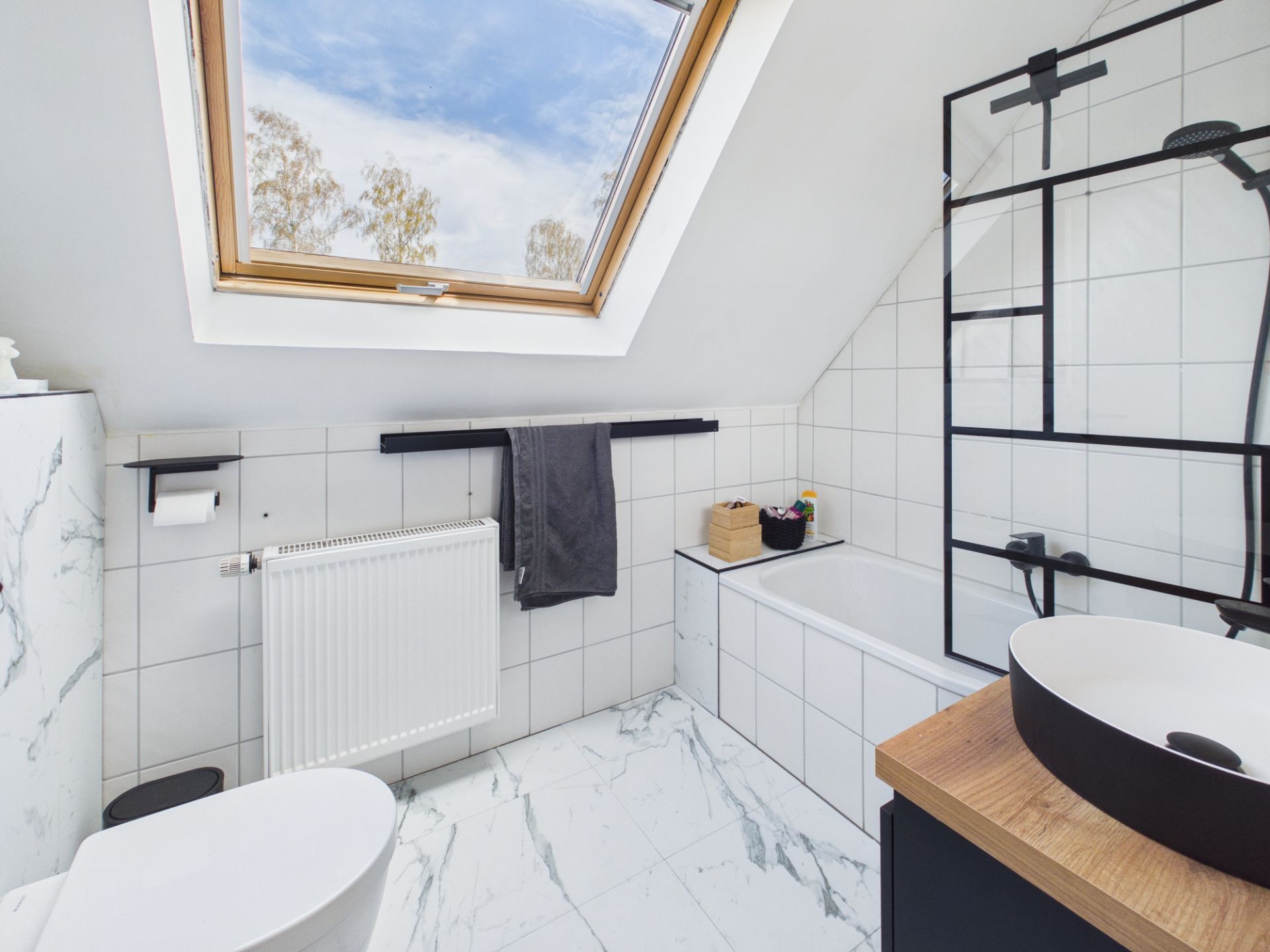 Modernes Badezimmer mit Dachfenster, Badewanne, Waschbecken und weißen Fliesen.