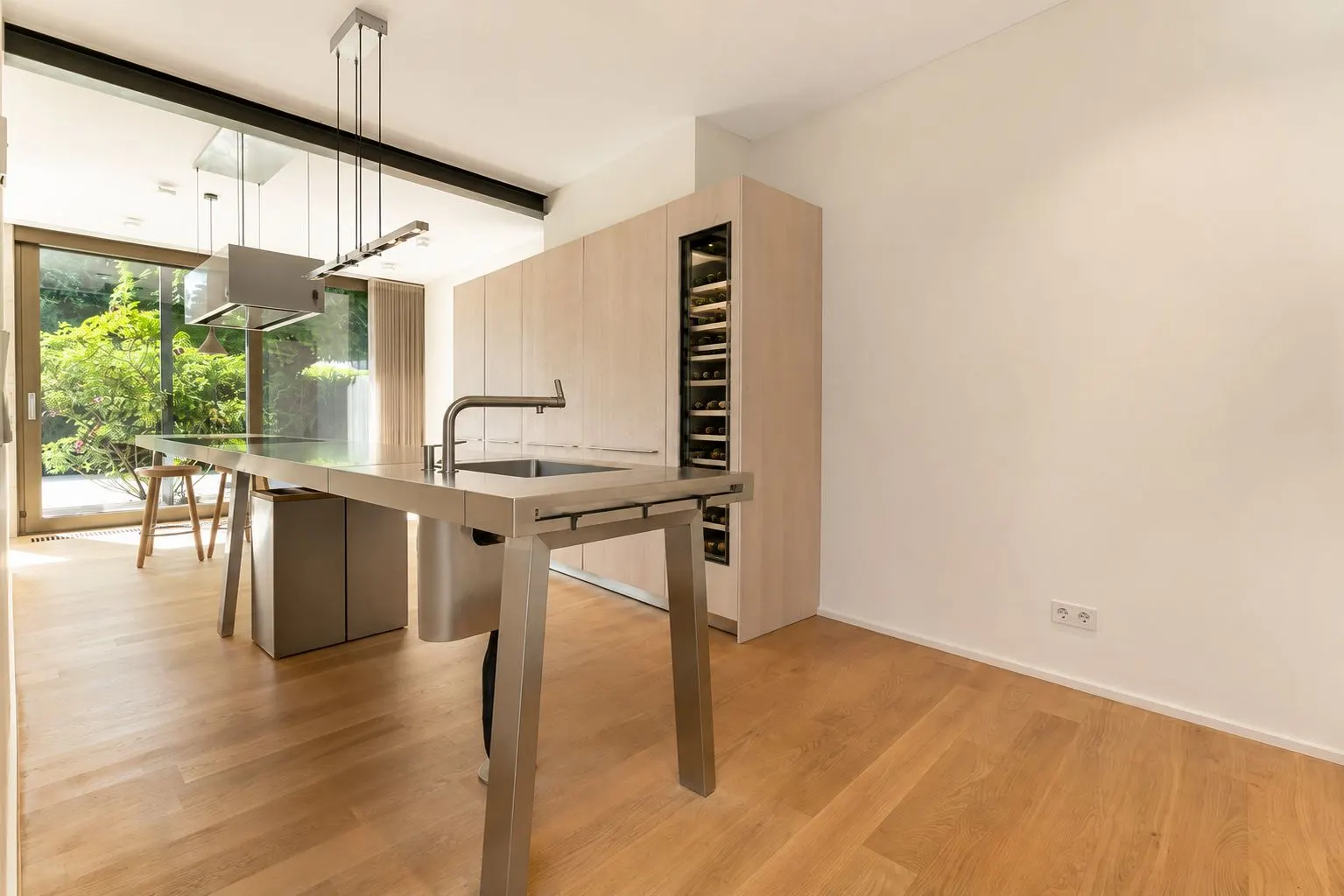 Moderne Küche mit Holzboden, Insel mit Spüle und Blick auf großen Fensterbereich zum Garten.