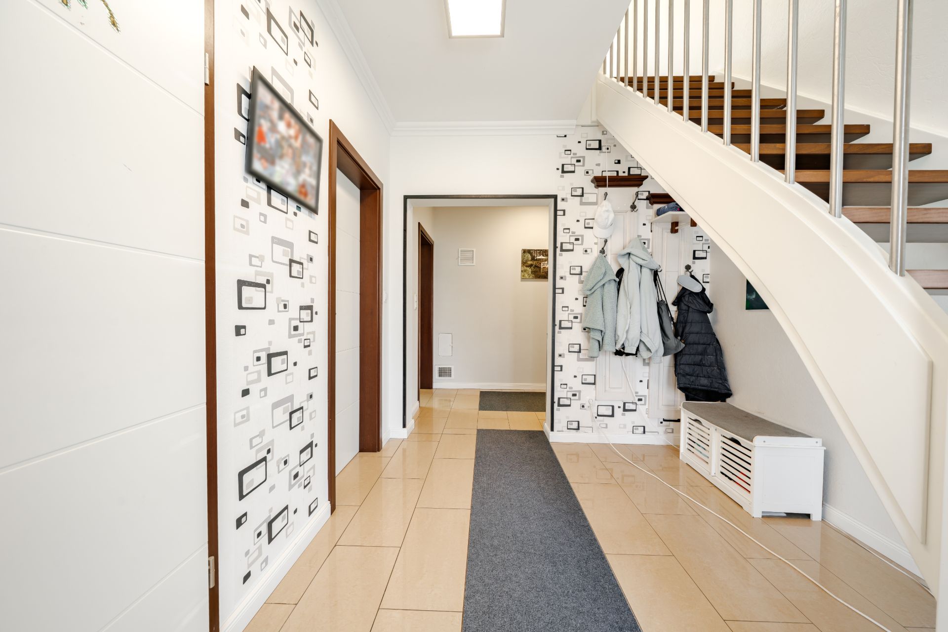 Heller Flur mit Treppe, Garderobe, Jacken und Sitzbank in einem Wohnhaus.