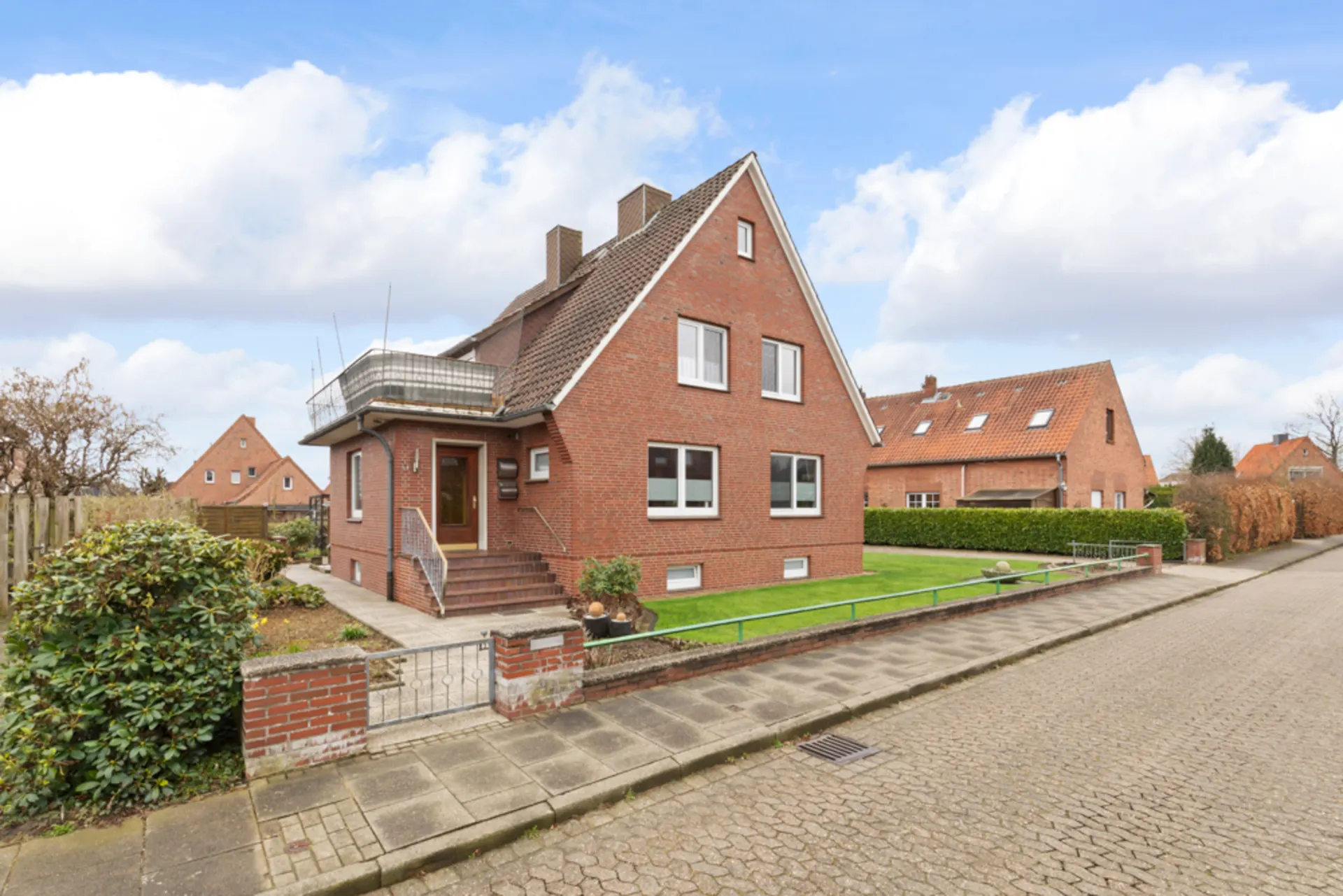 Backsteinhaus mit Vorgarten, Stufen zum Eingang und Balkon auf einer ruhigen Wohnstraße.