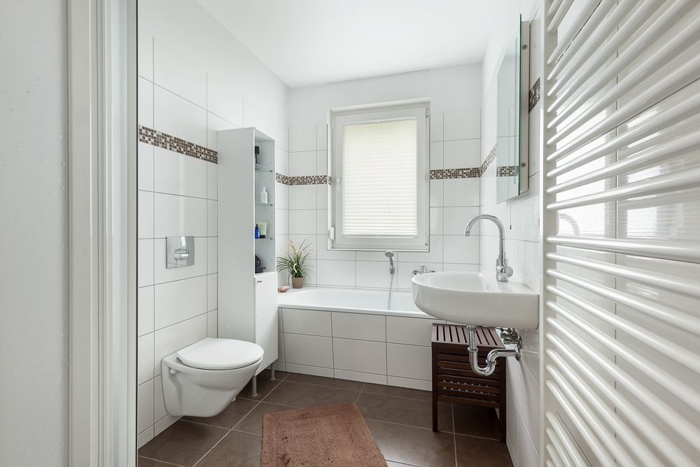 Modernes Badezimmer mit weißer Badewanne, Wandwaschbecken, WC und Fenster.