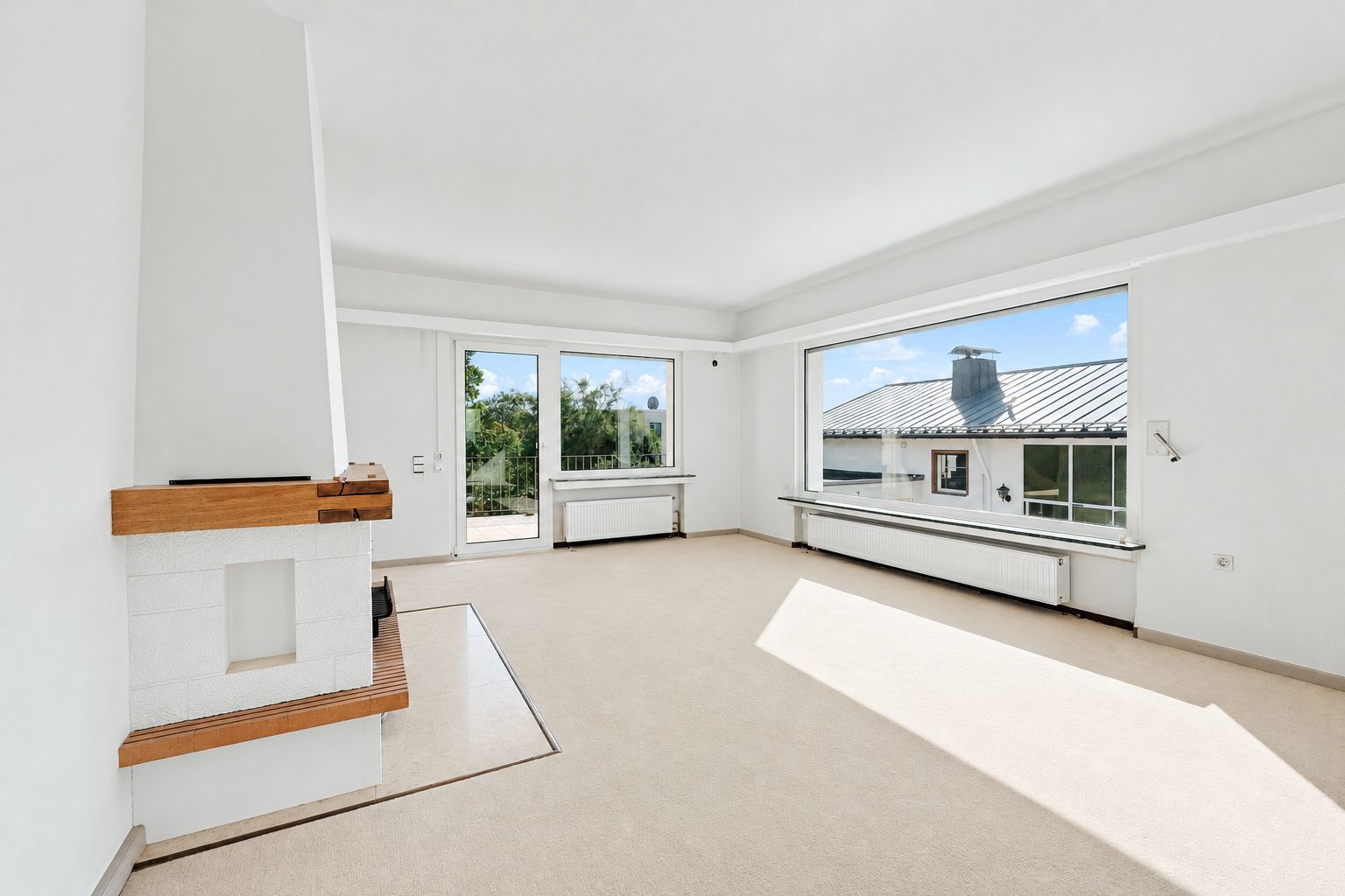 Helles Wohnzimmer mit Kamin, großem Fenster und Ausgang zur Terrasse.