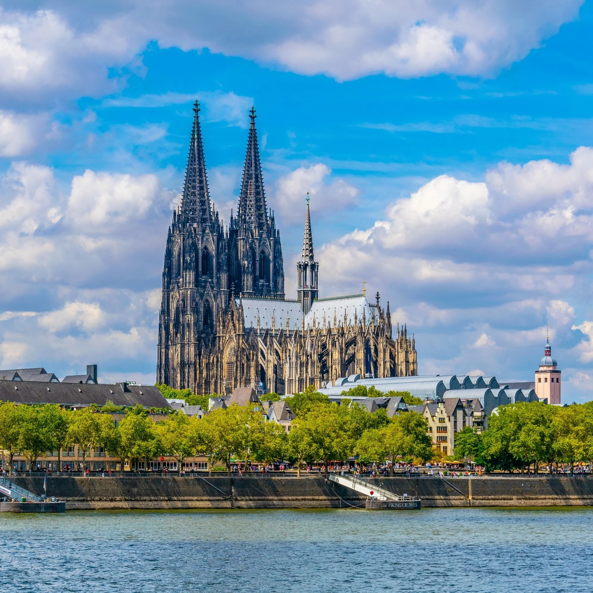 Blick auf eine große gotische Kathedrale und andere Gebäude am Flussufer mit Bäumen.