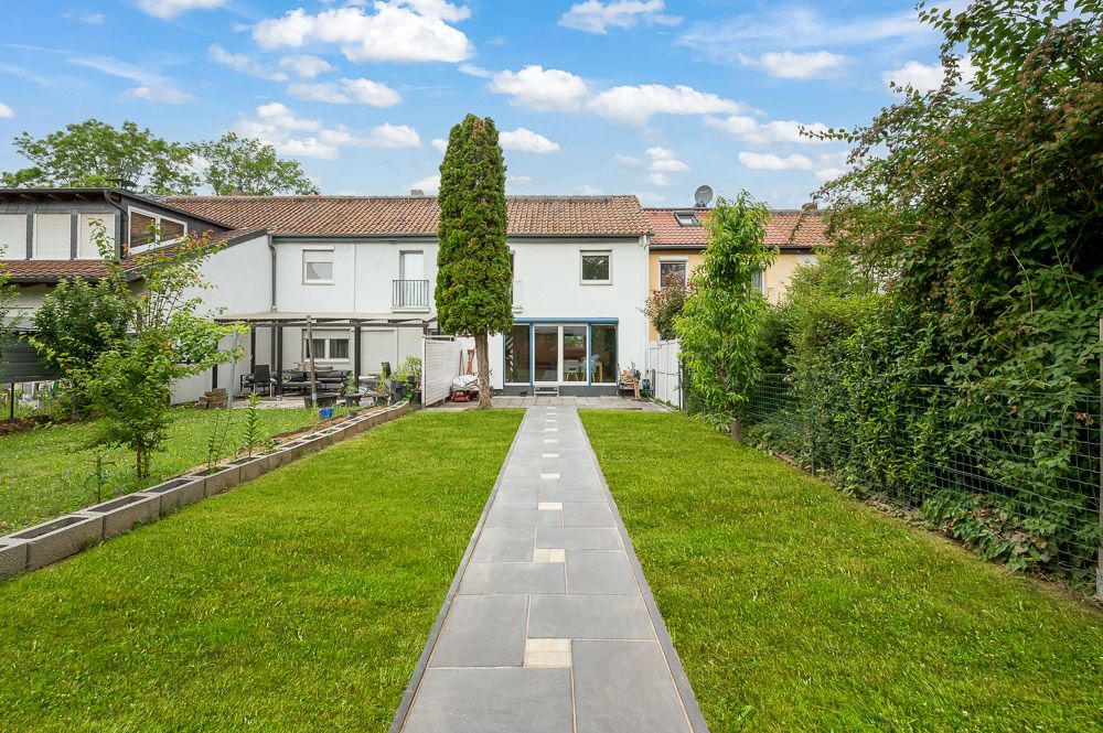 Gepflegter Garten mit Rasen, Weg und Blick auf ein weißes Wohnhaus mit Terrasse.