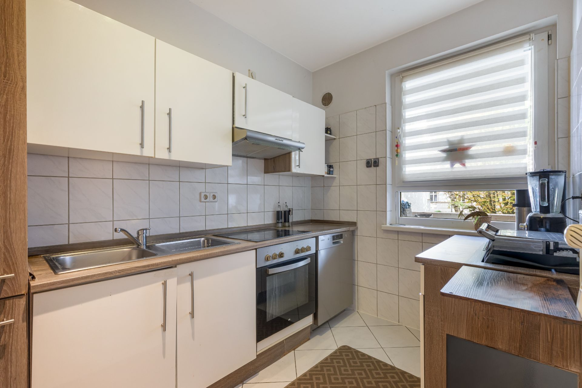 Moderne Küche mit Herd, Spüle, Arbeitsflächen und großem Fenster mit Jalousie.