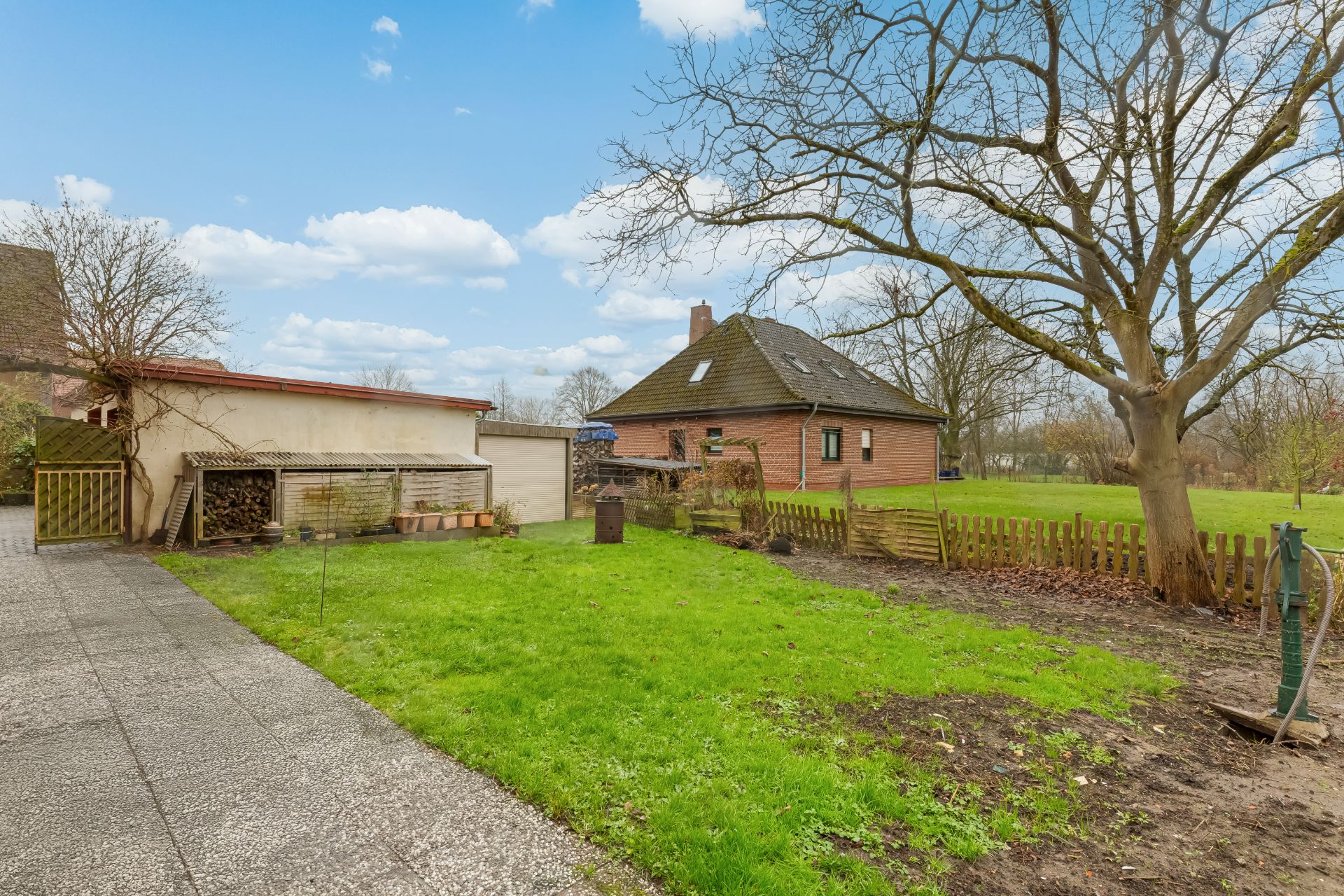 Garten mit grünem Rasen, großem Baum und Zaun, im Hintergrund ein rotes Wohnhaus und eine Garage.