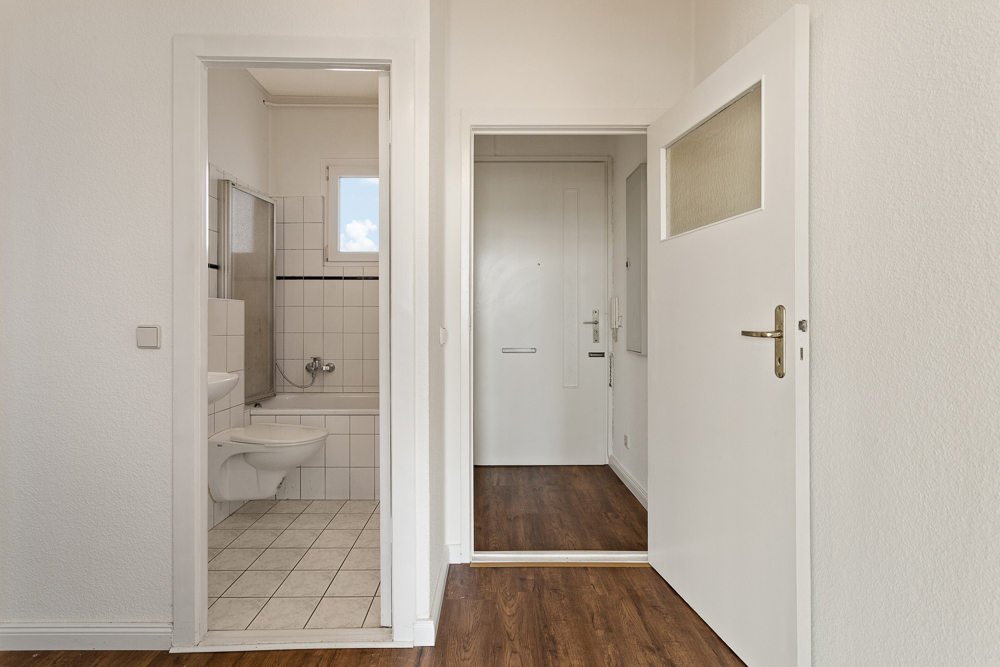 Blick auf einen Flur mit Holzboden und ein angrenzendes Badezimmer mit Badewanne.