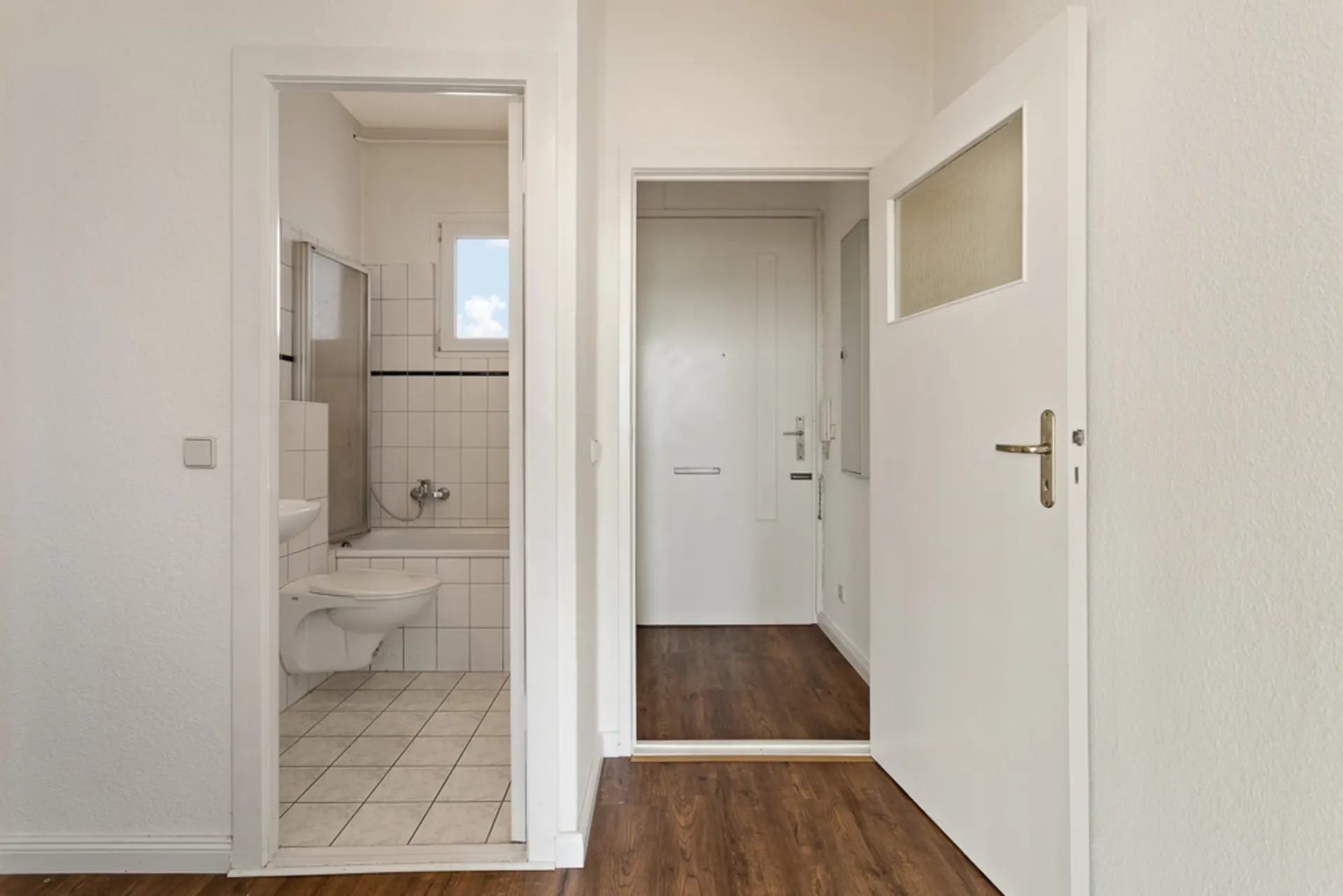 Blick auf einen Flur mit Holzboden und ein angrenzendes Badezimmer mit Badewanne.