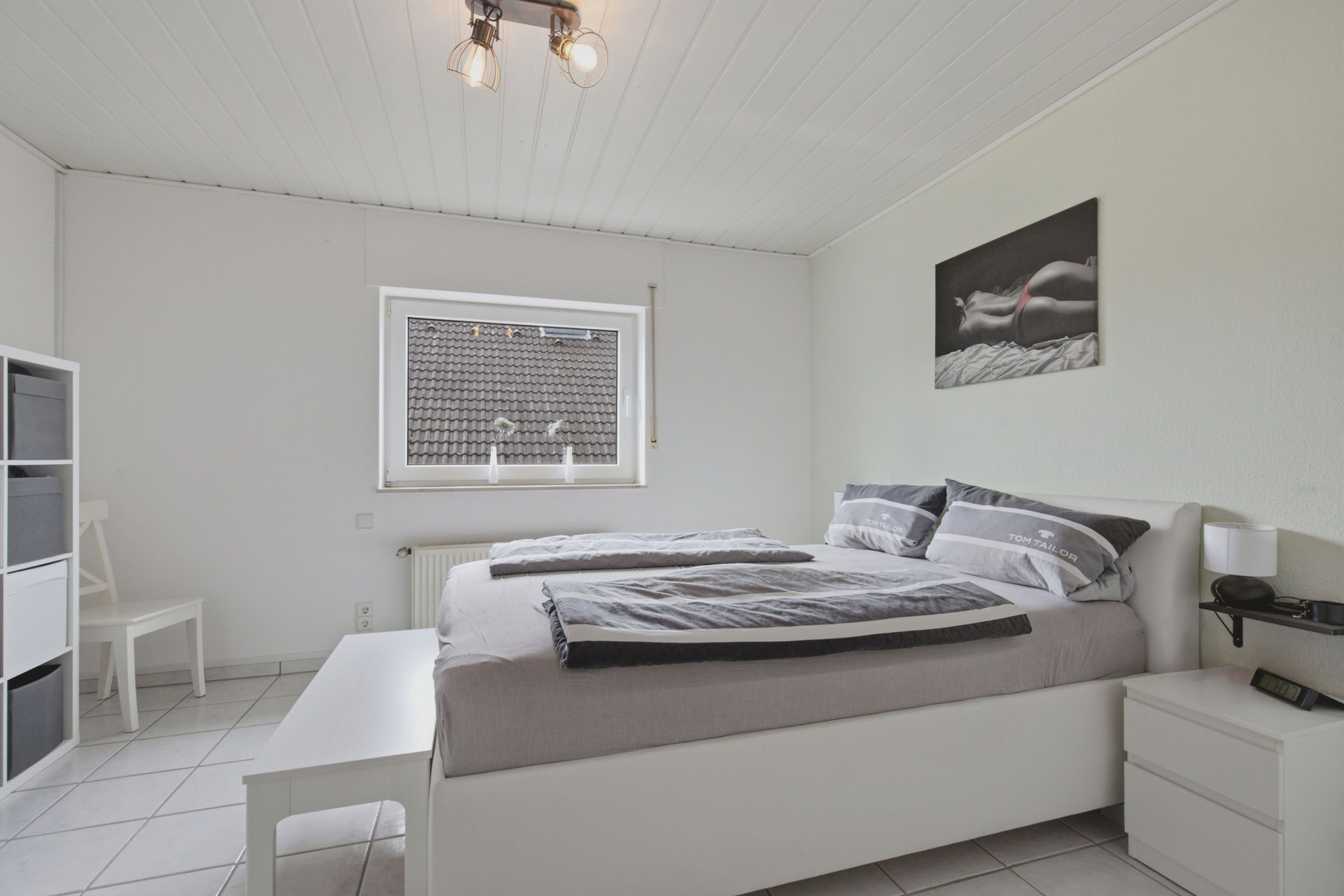 Helles Schlafzimmer mit Doppelbett, Nachttisch, Fenster und Wandbild.