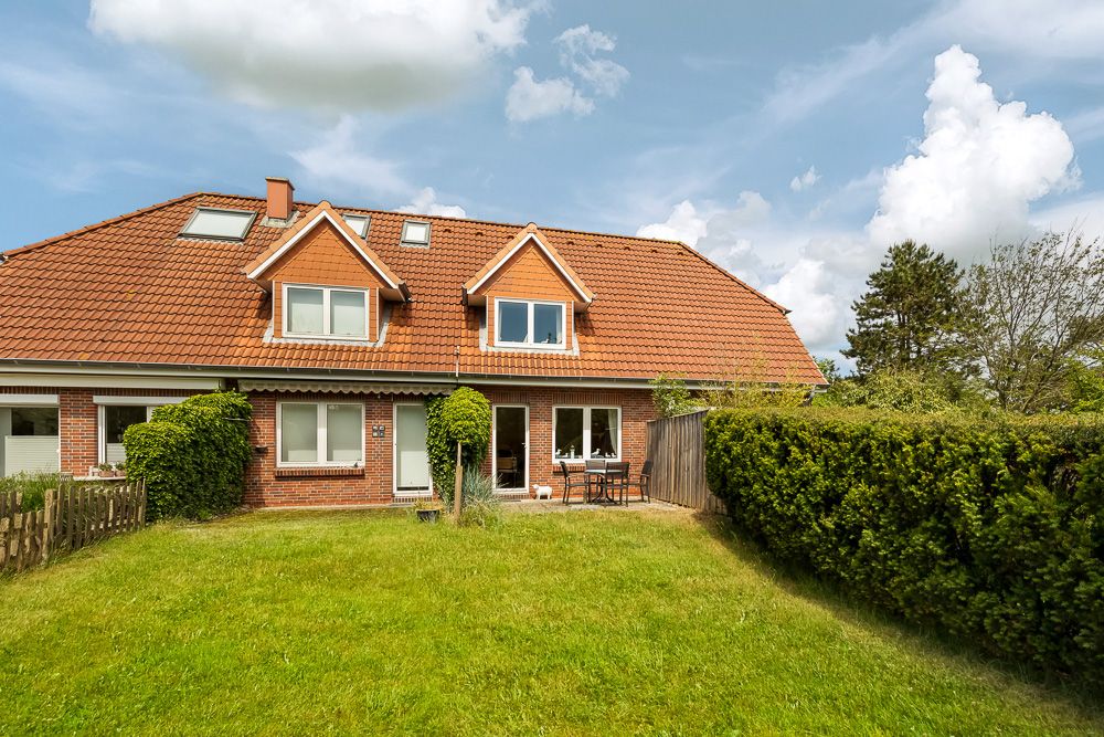 Zweistöckiges Backsteinhaus mit rotem Dach und Garten, Gartenmöbel auf Terrasse sichtbar.