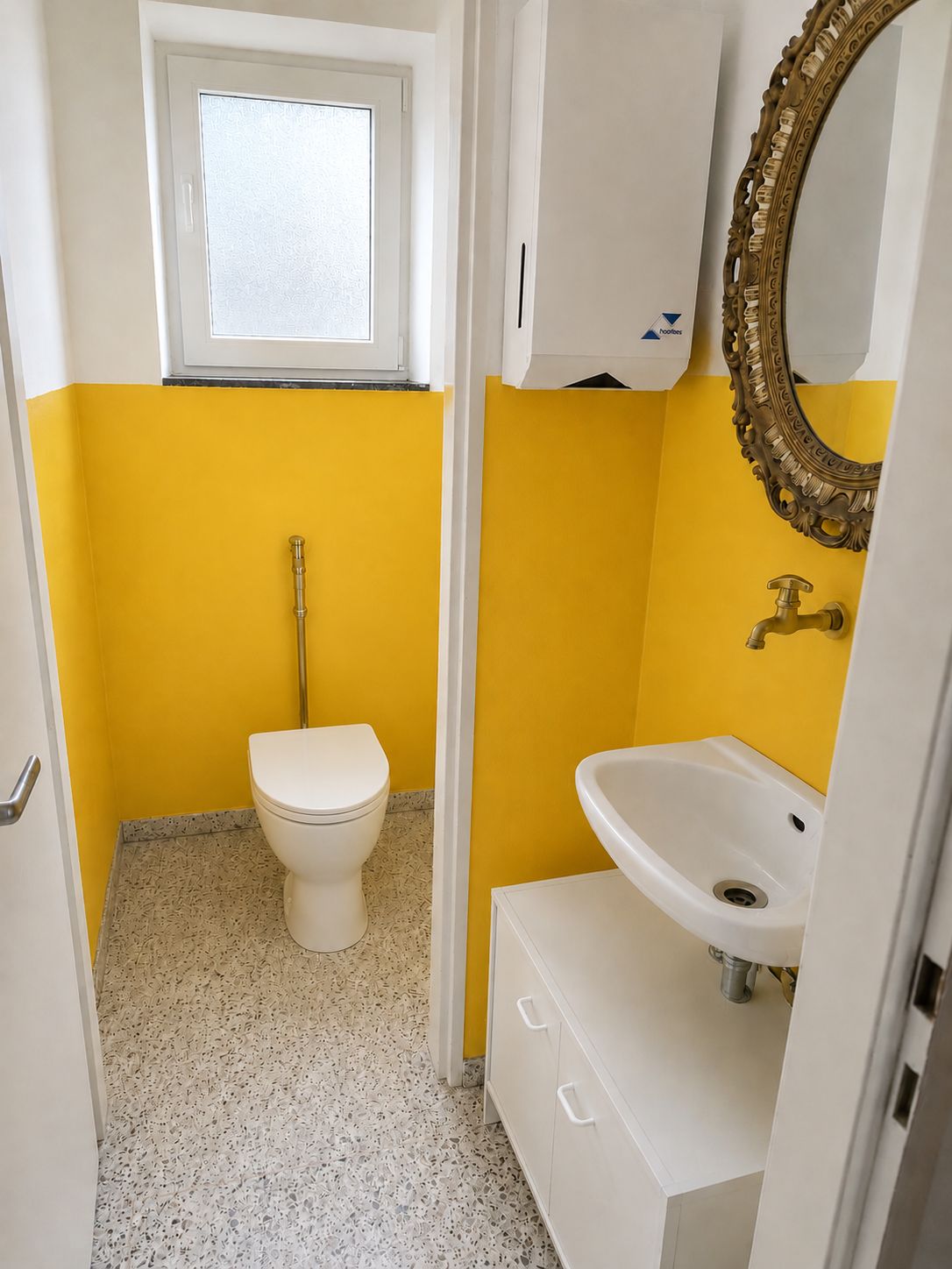 Kleines Badezimmer mit gelber Wand, Toilette, Waschbecken, Spiegel und Fenster.