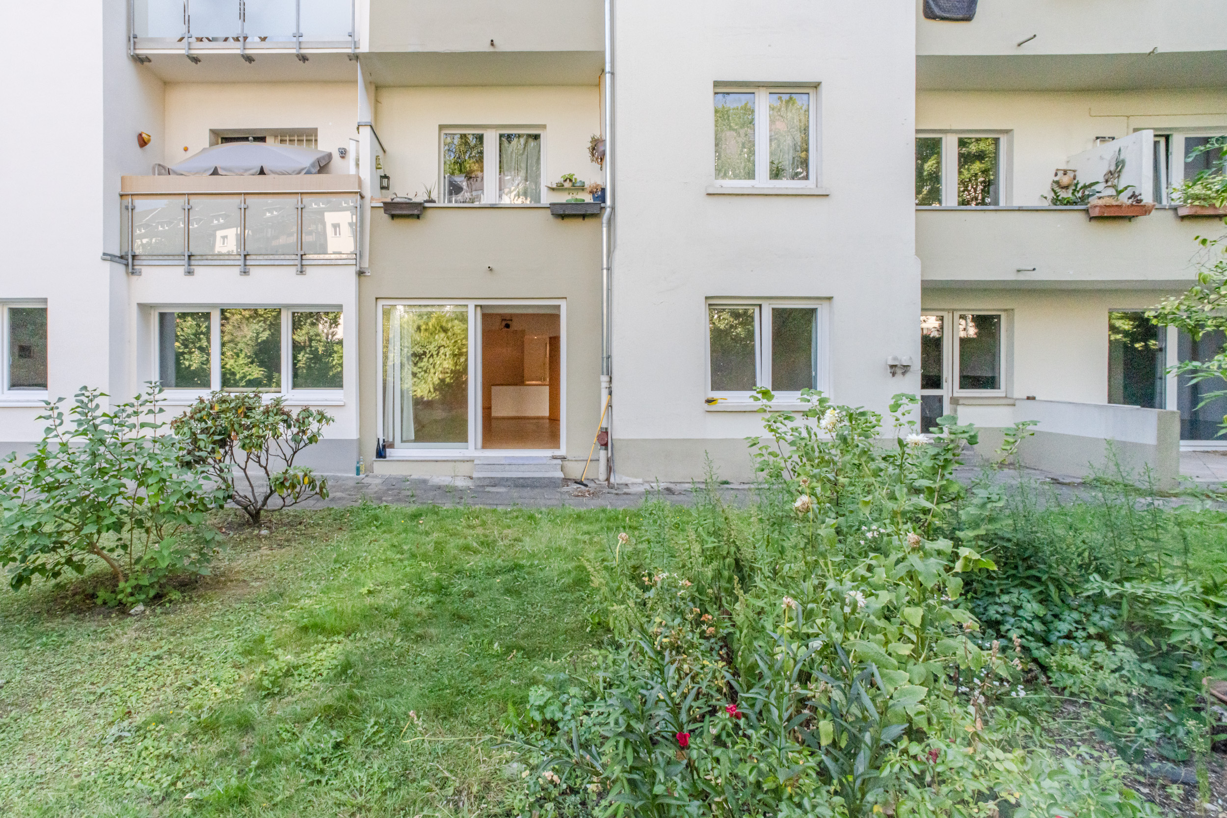 Rückseite eines Wohnhauses mit Terrasse, Garten und bodentiefen Fenstern.