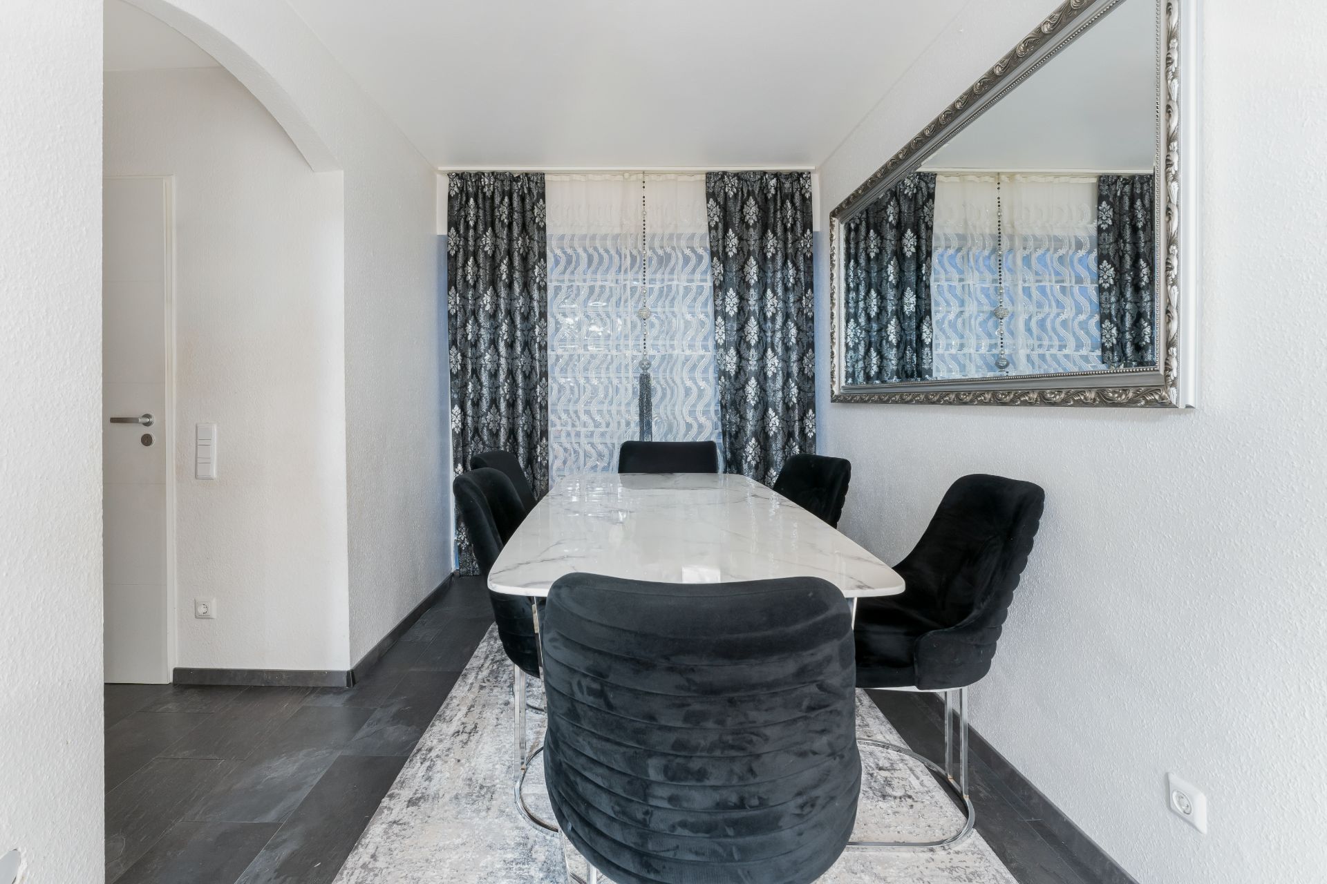 Esszimmer mit weißem Tisch, sechs schwarzen Stühlen und großem Wandspiegel.