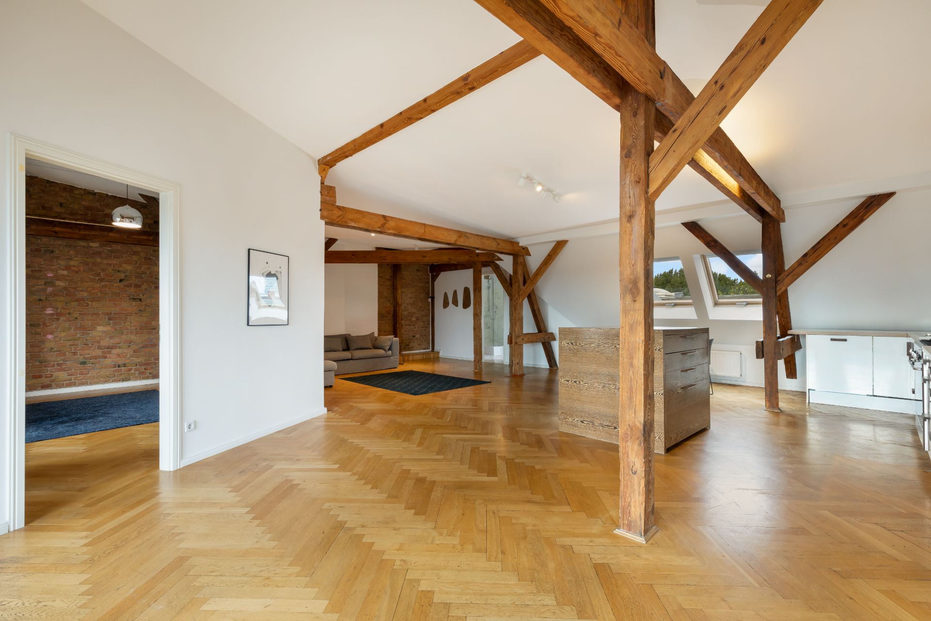 Geräumiger Wohnbereich mit Holzbalken, Parkettboden, Sofa und moderner Küche.