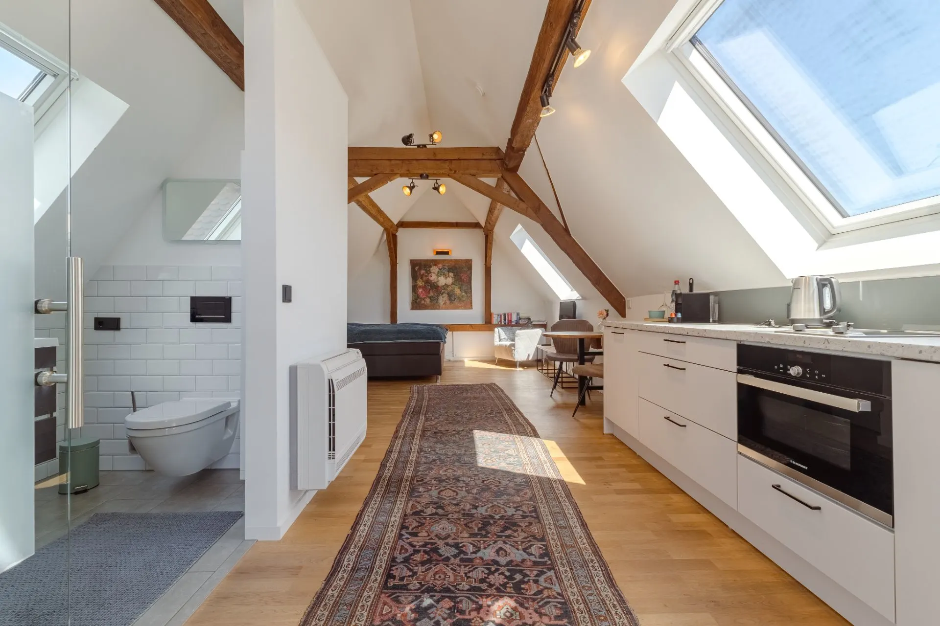Modernes Dachgeschoss mit Küche, Bad, sichtbaren Holzbalken und großen Dachfenstern.