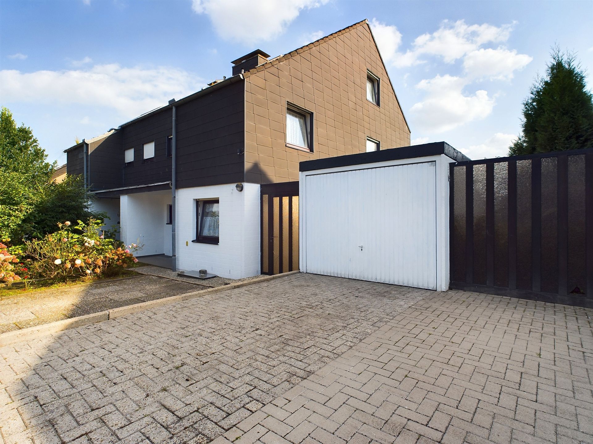 Einfamilienhaus mit Garage und gepflasterter Einfahrt, umgeben von Büschen.