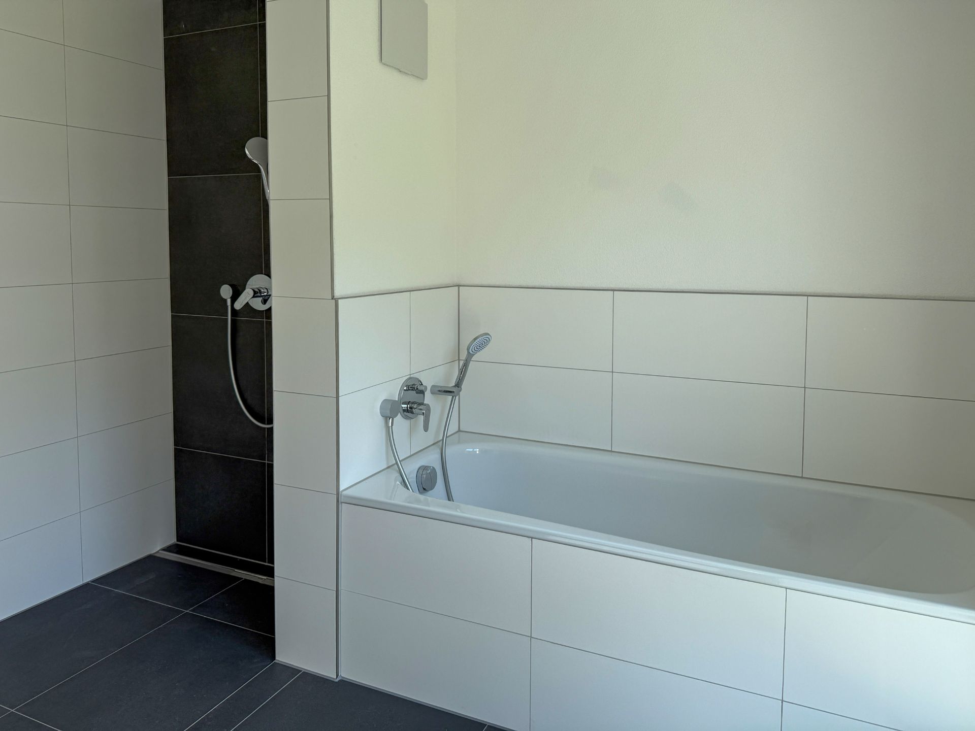 Modernes Badezimmer mit Badewanne und offener Dusche, weiße Fliesen an den Wänden.