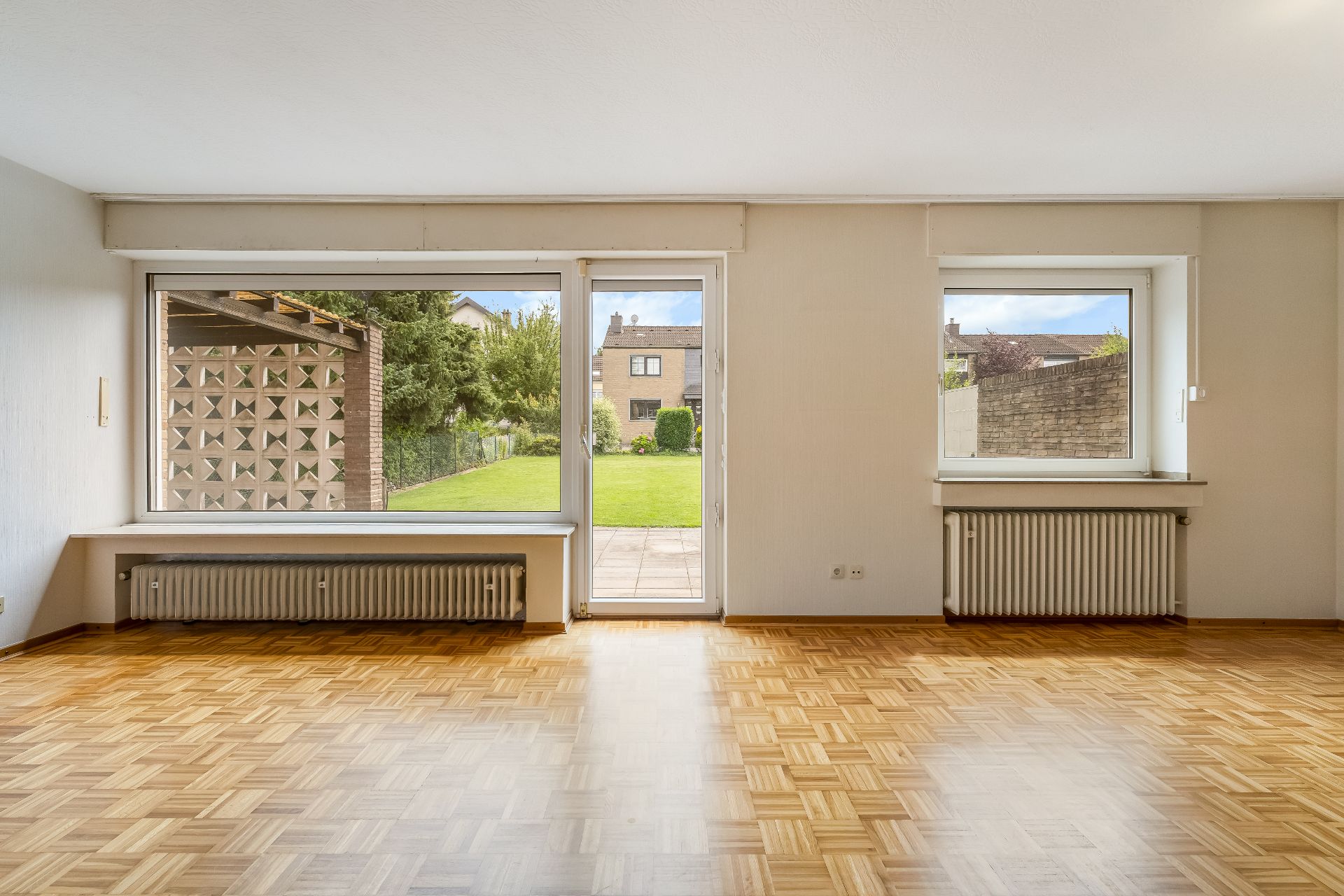 Helles Wohnzimmer mit Parkettboden, großen Fenstern und Blick in einen Garten.