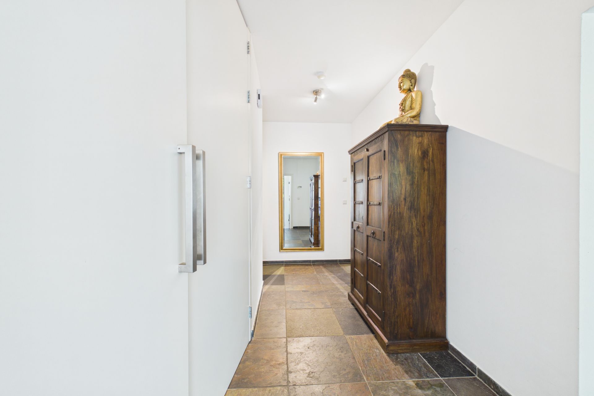 Heller Flur mit braunem Schrank, großem Spiegel und einer Buddha-Statue.