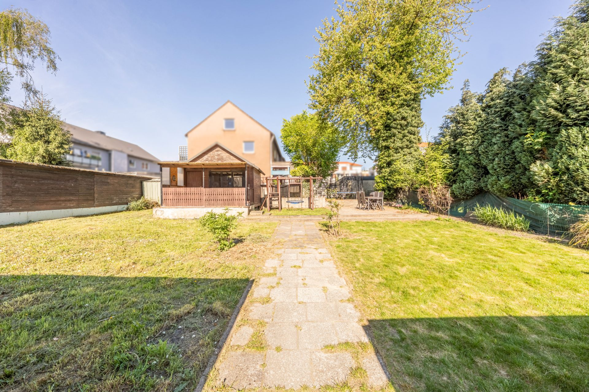 Garten mit gepflastertem Weg, Rasenfläche, Holzpavillon und Sitzbereich, Einfamilienhaus im Hintergrund.